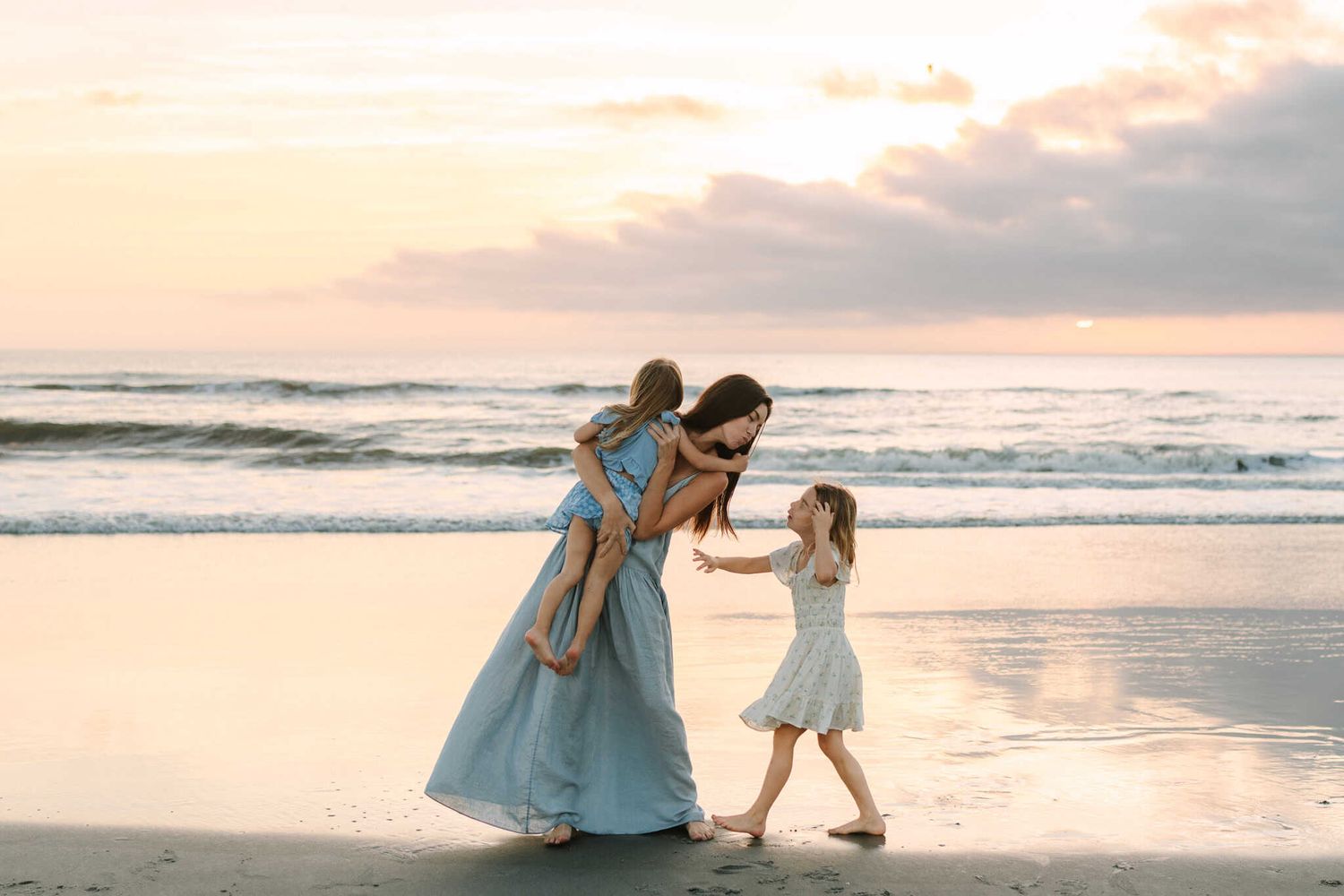 mom and daughters playing with their toes in the ocean on the beach