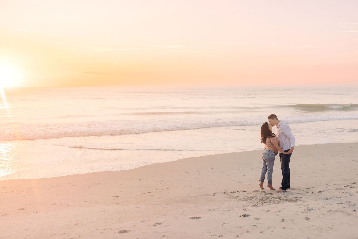 pregnant couple kissing at sunrise