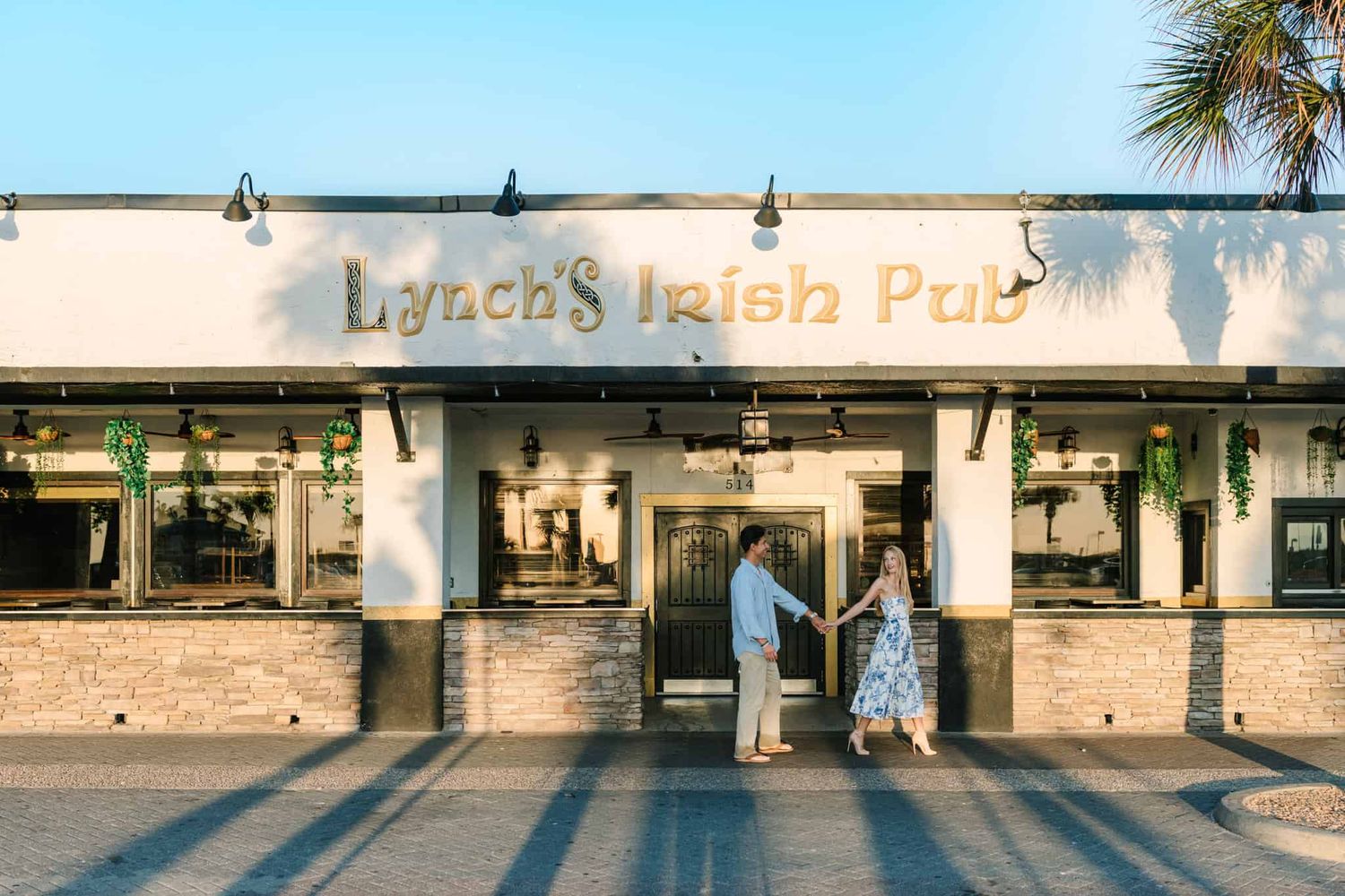 Couple holding hands in front of Lynch's Irish Pub entrance, bathed in warm golden hour sunlight.