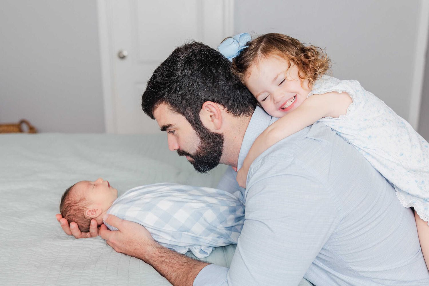 dad holding newborn baby while older toddler girl lays on his back with big smile