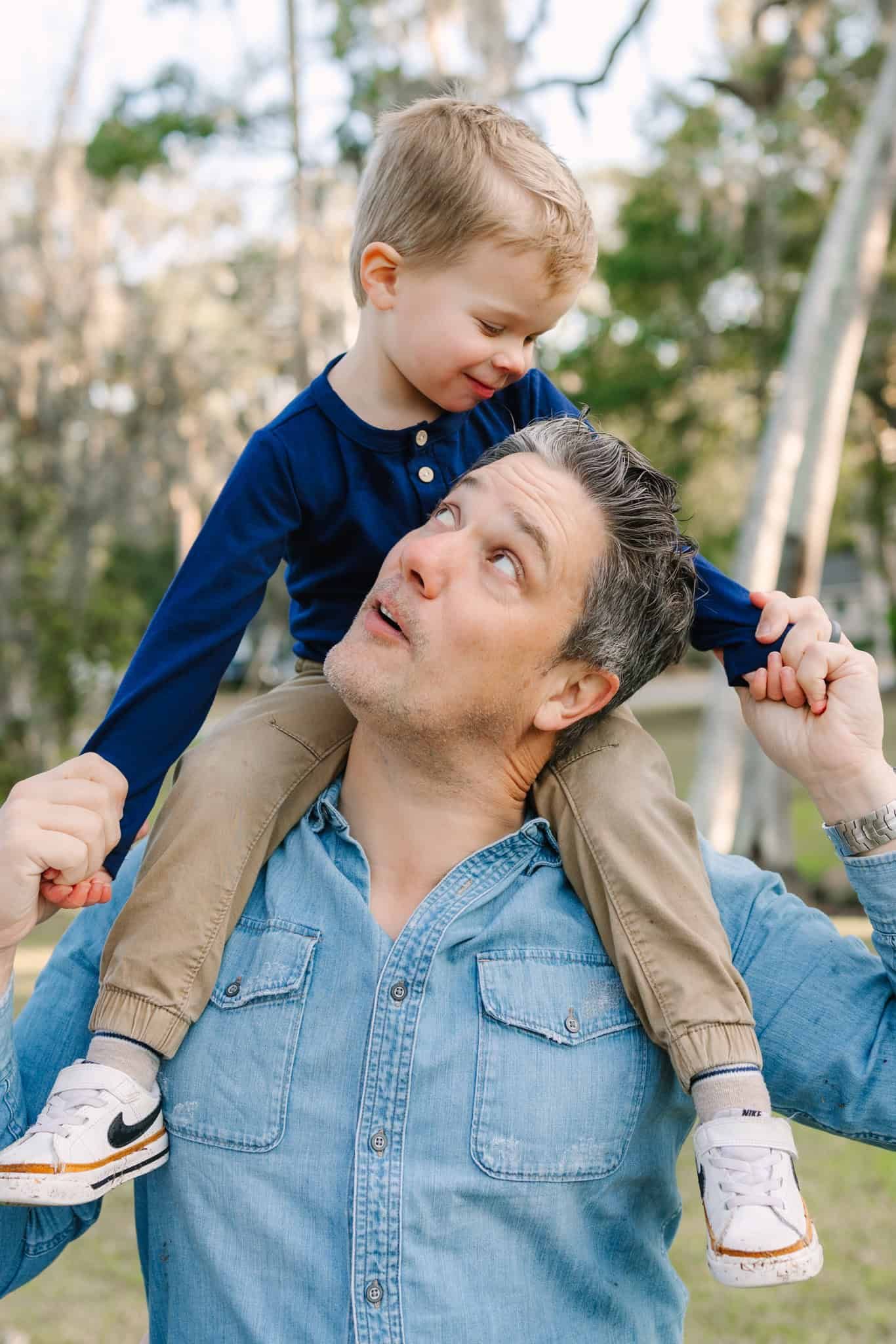 son sitting on dads shoulders with them looking at each other and smiling