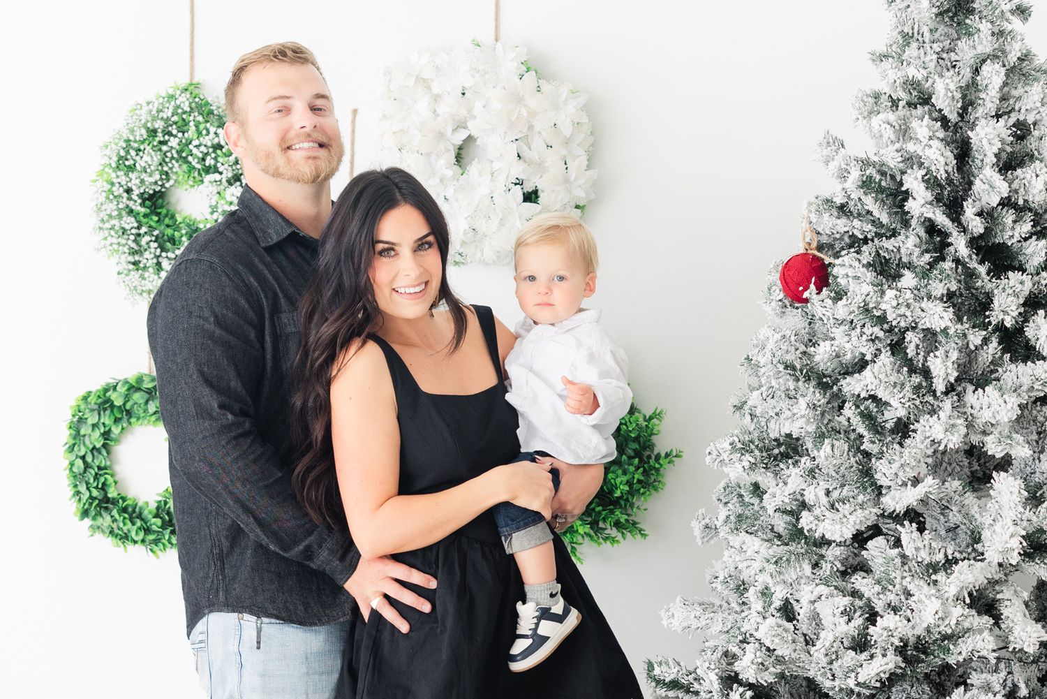 family of three at Christmas studio mini session setup with wreaths behind them