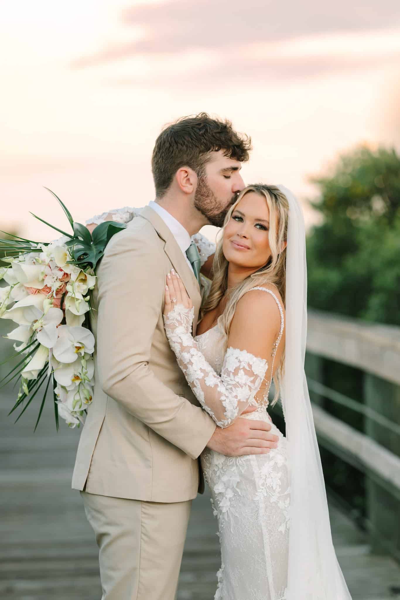 bride smiling and holding bouquet while groom gives her a kiss on her temple