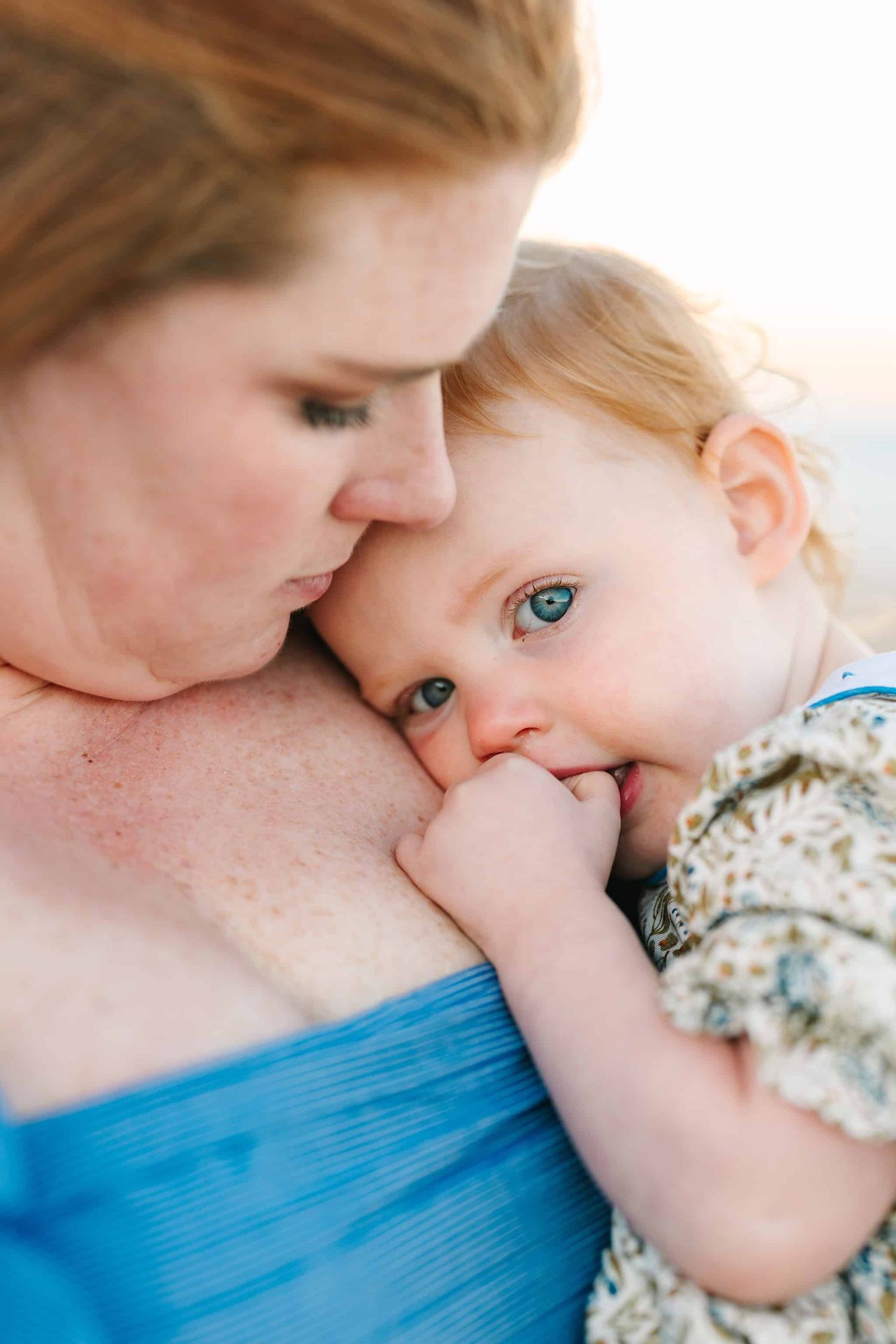 baby girl snuggling into mom with her bright blue eyes and red hair
