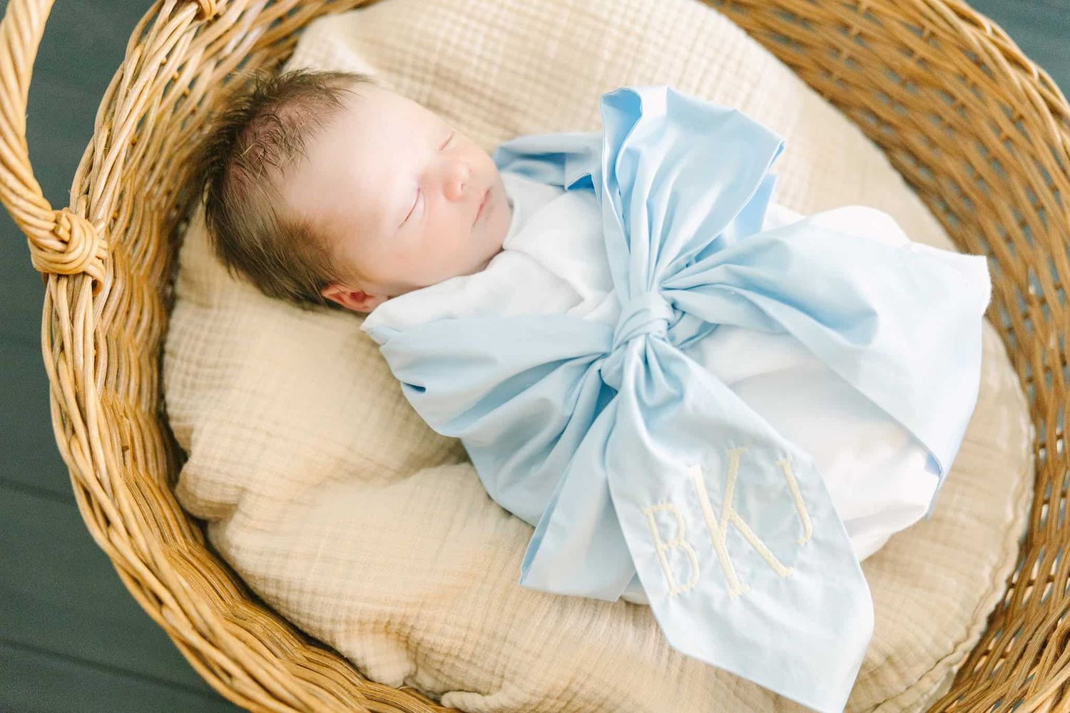 newborn baby boy swaddled with a blue bow laying in a basket
