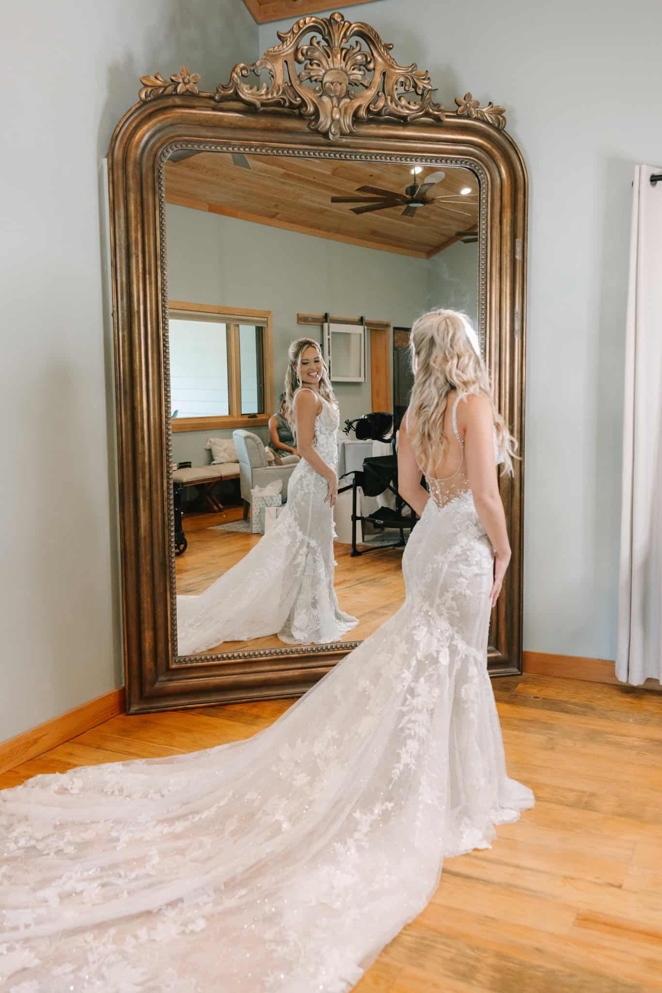 bride standing in front of a large mirror looking at it and her train out behind her