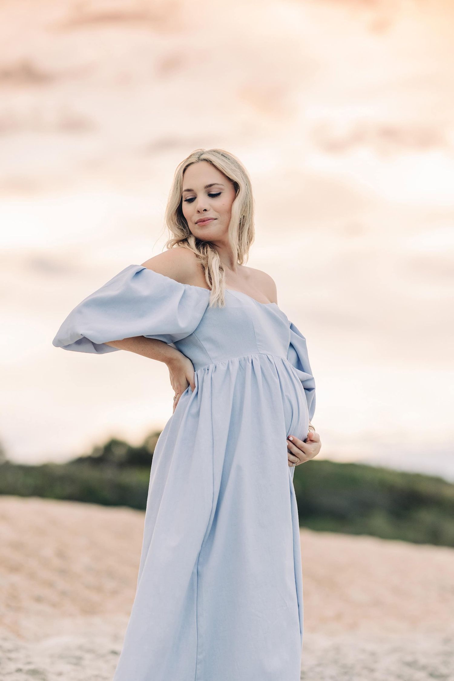 pregnant mama standing on the beach at sunset holding her belly and looking back