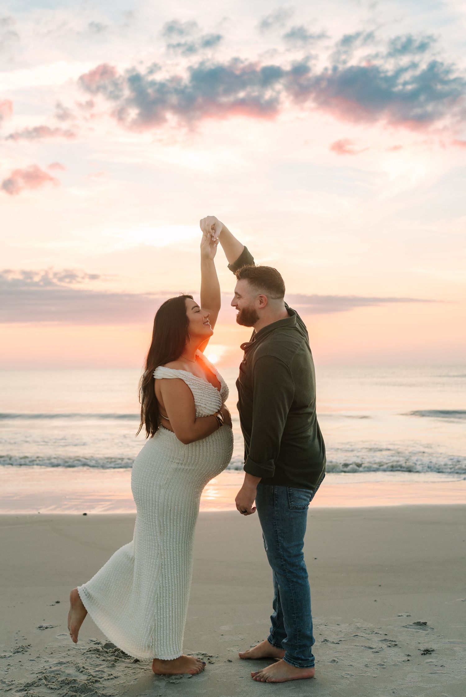 Pregnant couple dancing on jacksonville beach at sunrise, woman in white dress, man in dark shirt and jeans, ocean backdrop