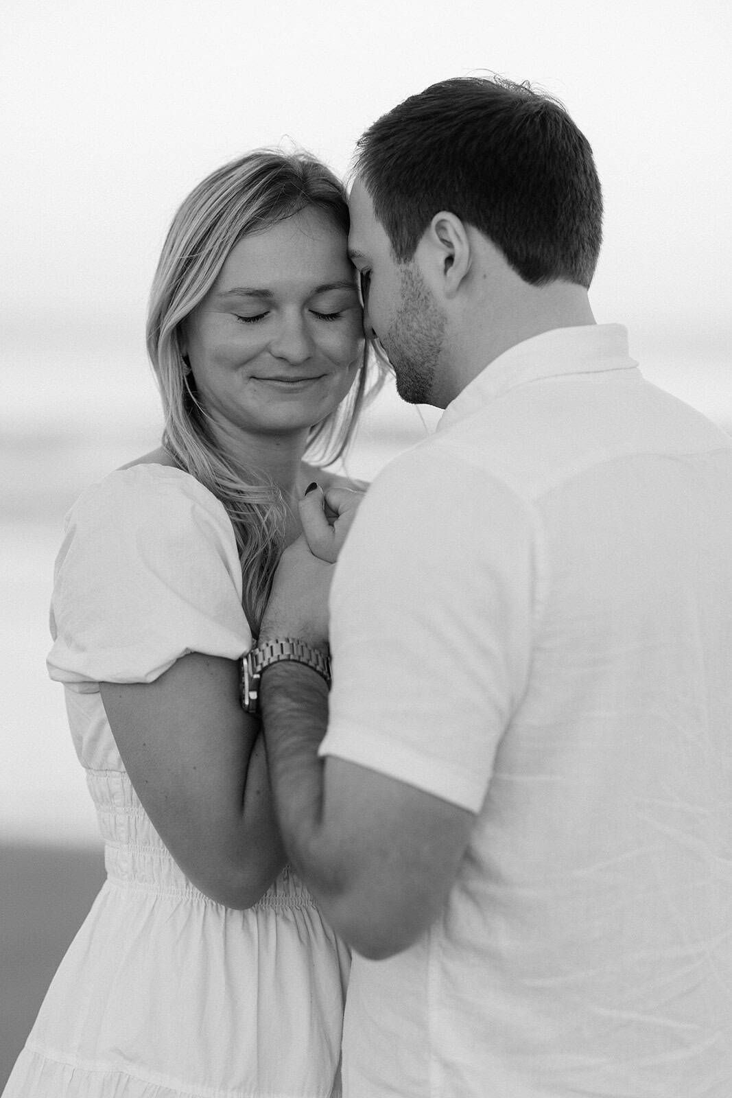 Black and white photo of a romantic couple embracing on a beach, woman smiling with eyes closed.
