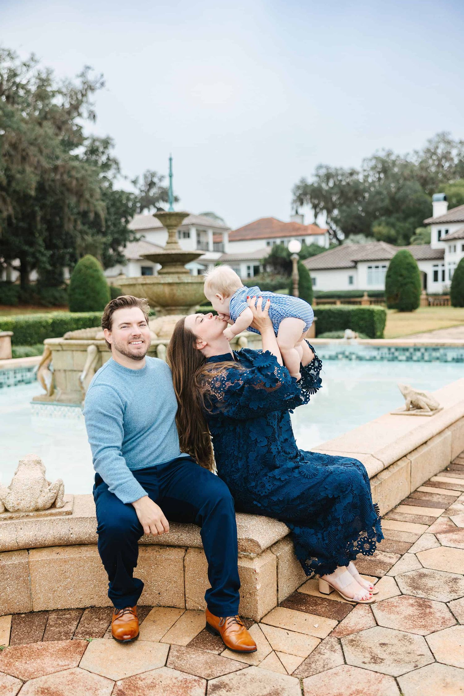 mom and dad playing with baby boy sitting by a fountain in Jacksonville, fl