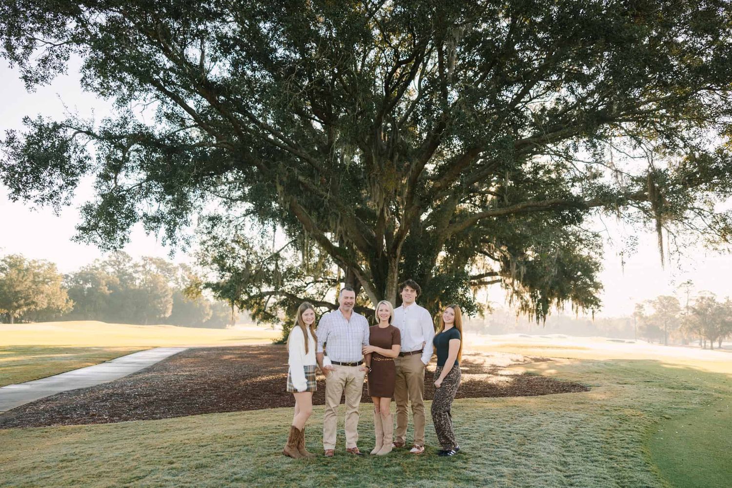 three teen children with mom and dad smiling with a big beautiful tree behind them at Jacksonville fl golf course