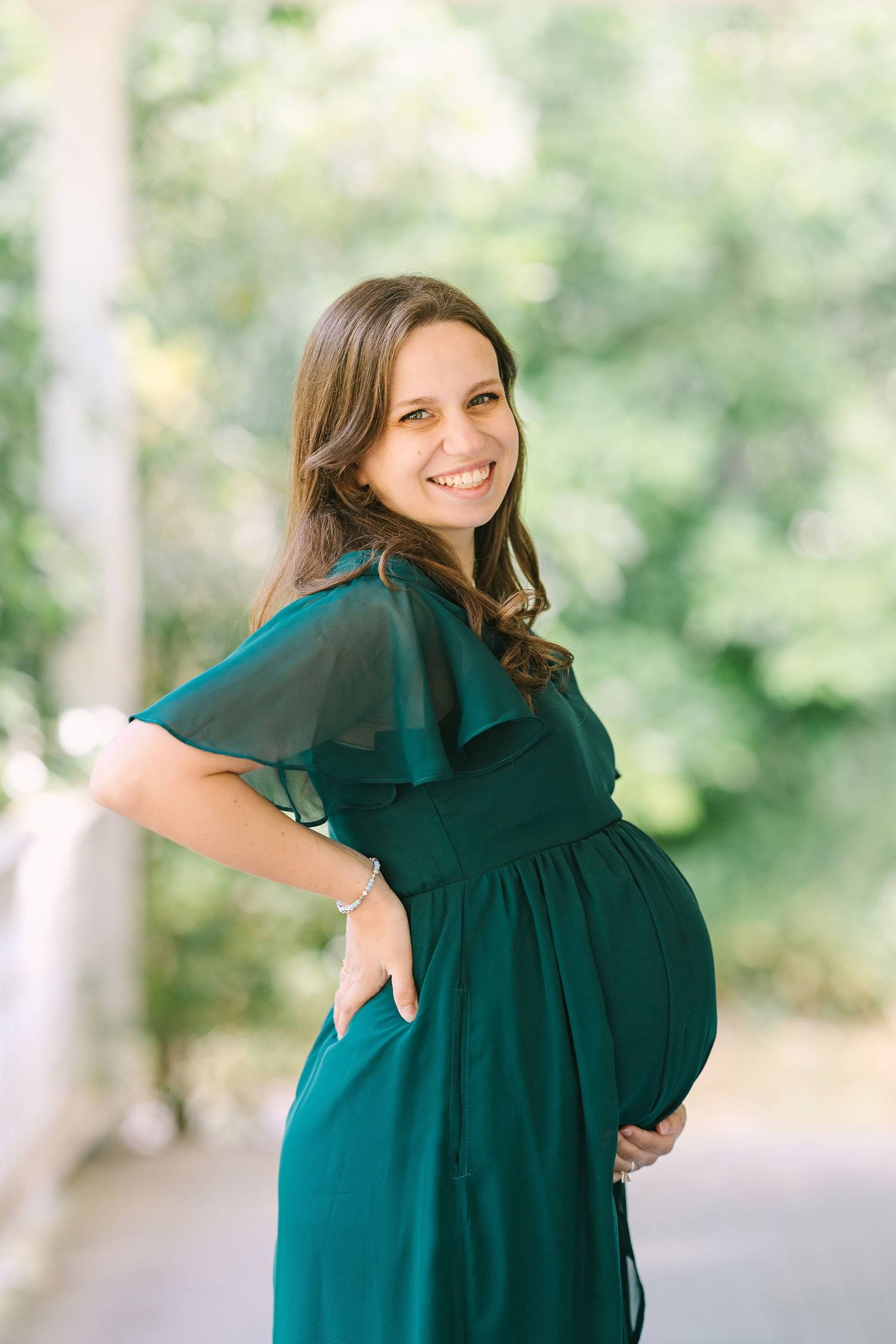 pregnant mom during maternity session in green dress on white porch smiling at the camera