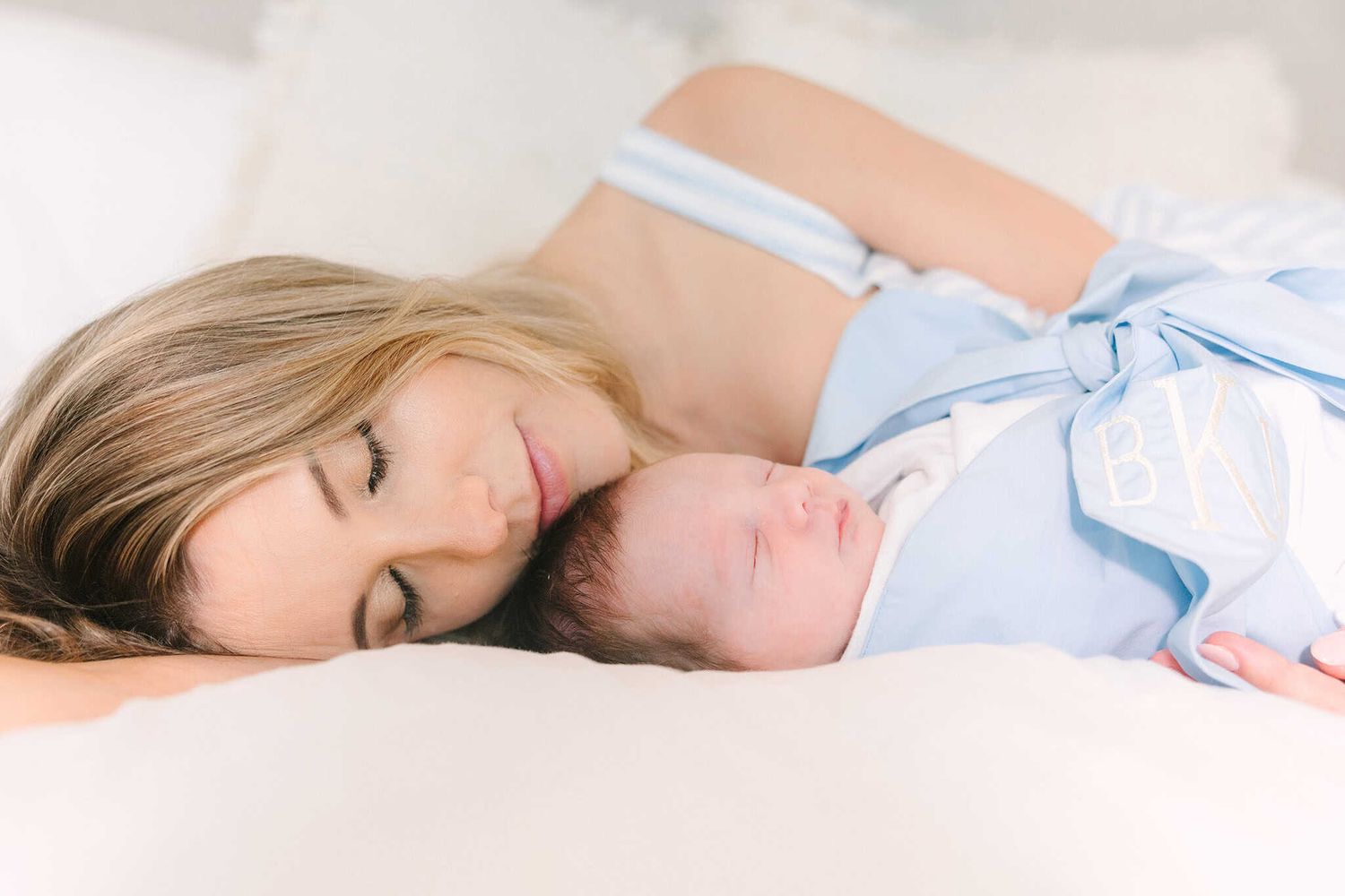 close up of mom laying on her side snuggling newborn baby boy swaddled with a blue bow