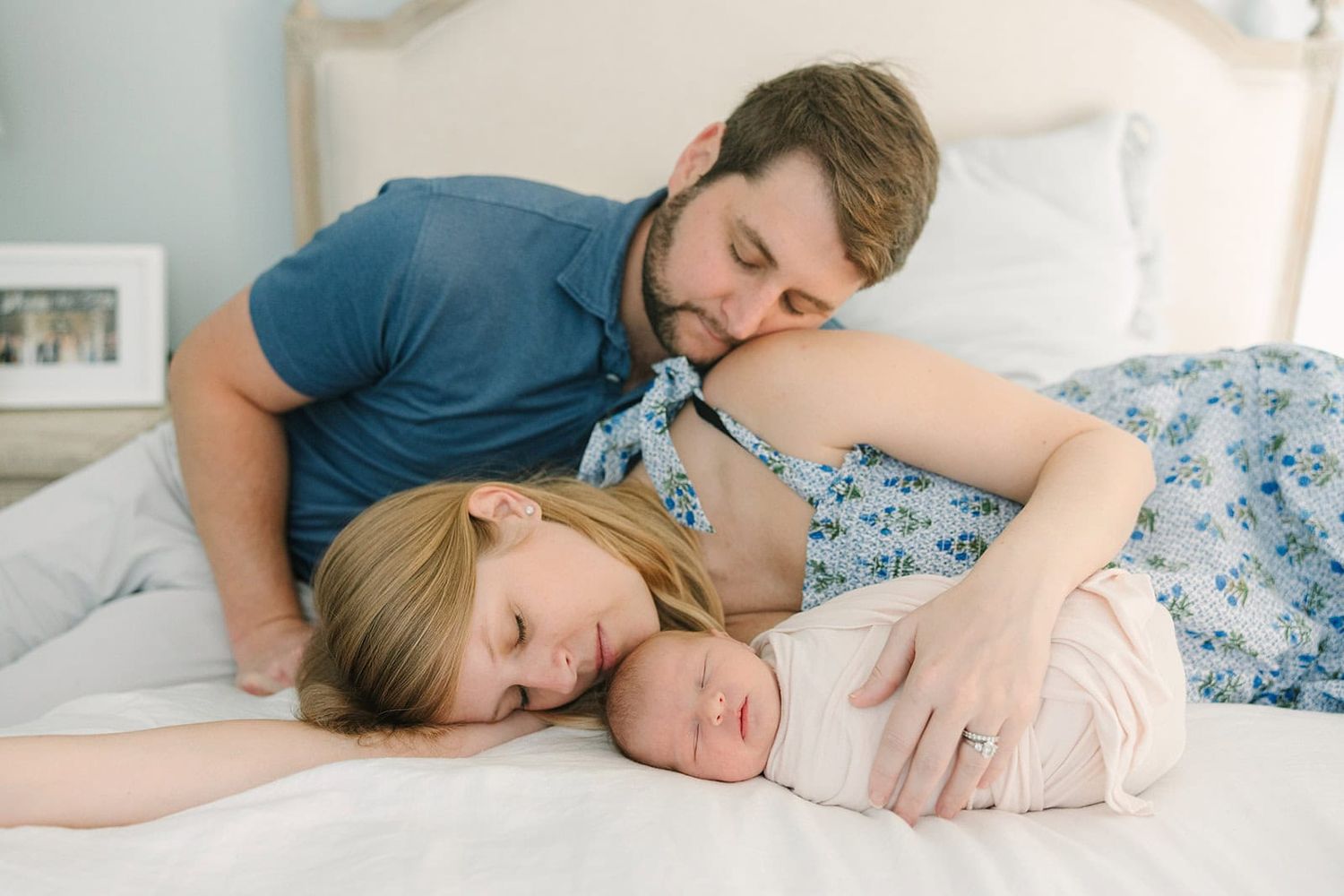 mom and dad laying on bed snuggling their swaddled newborn baby in Jacksonville fl