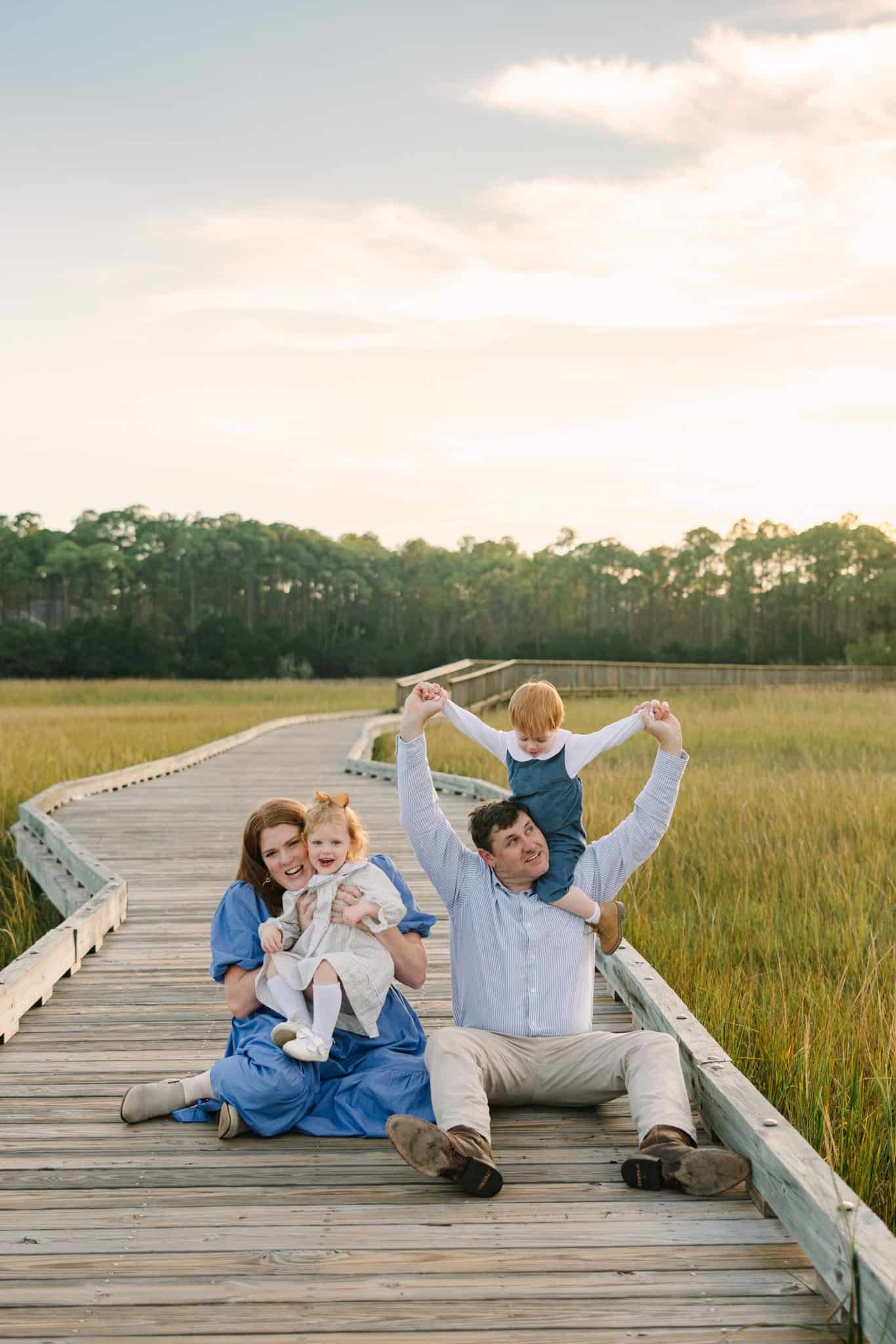 sitting on a boardwalk in st Augustine with son on dads shoulders and daughter laughing with mom at sunset