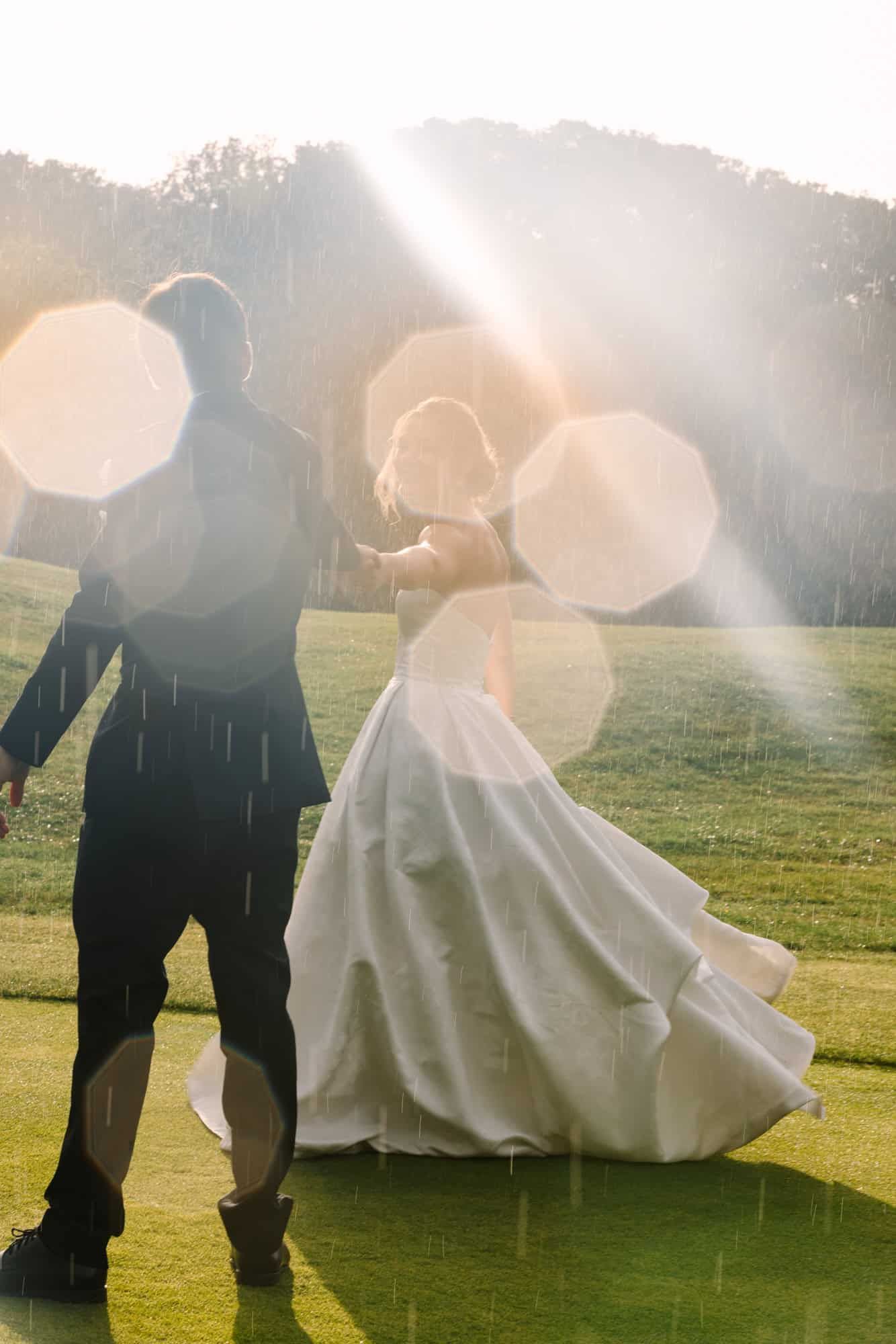 bride and groom dancing in the rain with sun flares