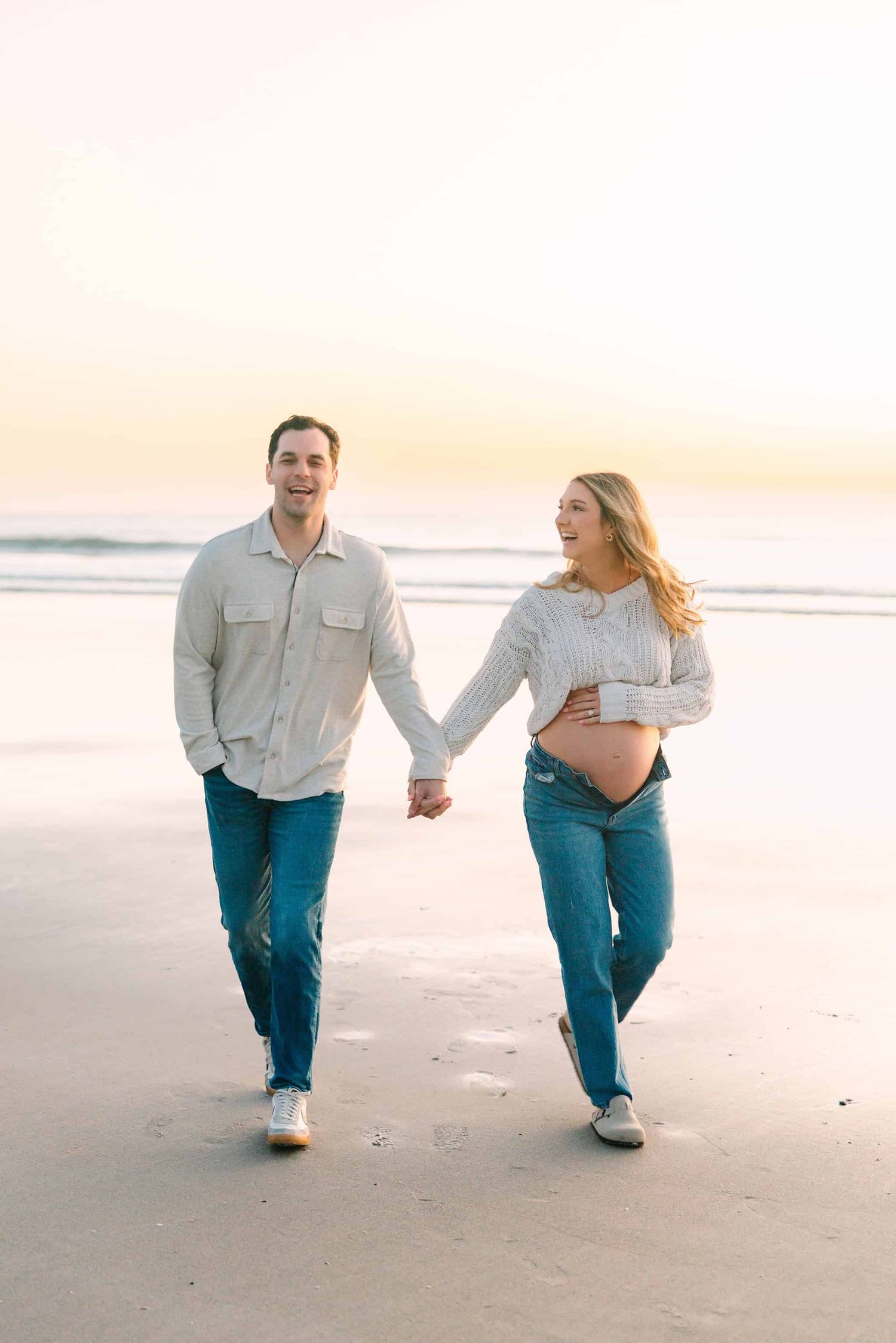 pregnant mom and husband walking down the beach at sunrise