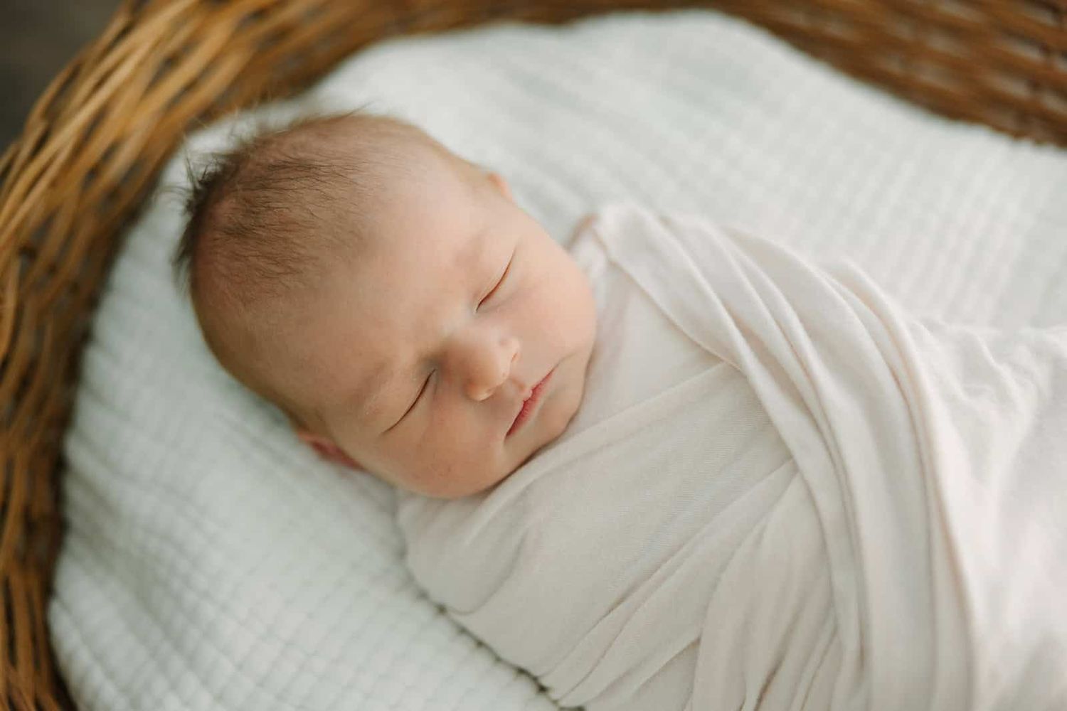 newborn baby swaddled laying in a basket face up with light coming from the side onto the baby's face