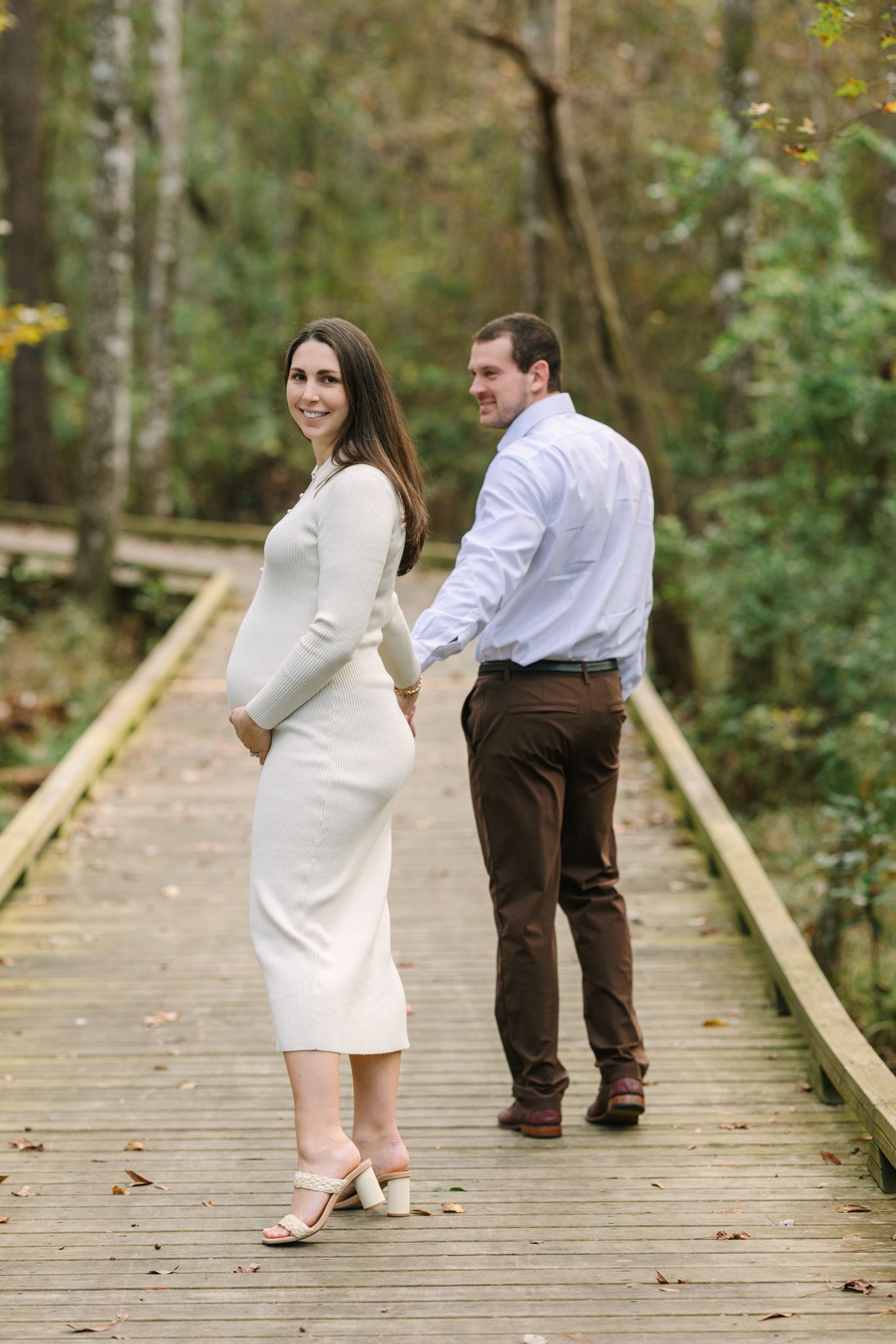 Jacksonville fl photographer of pregnant mom looking back over her shoulder with belly poking out as husband walks her down the boardwalk