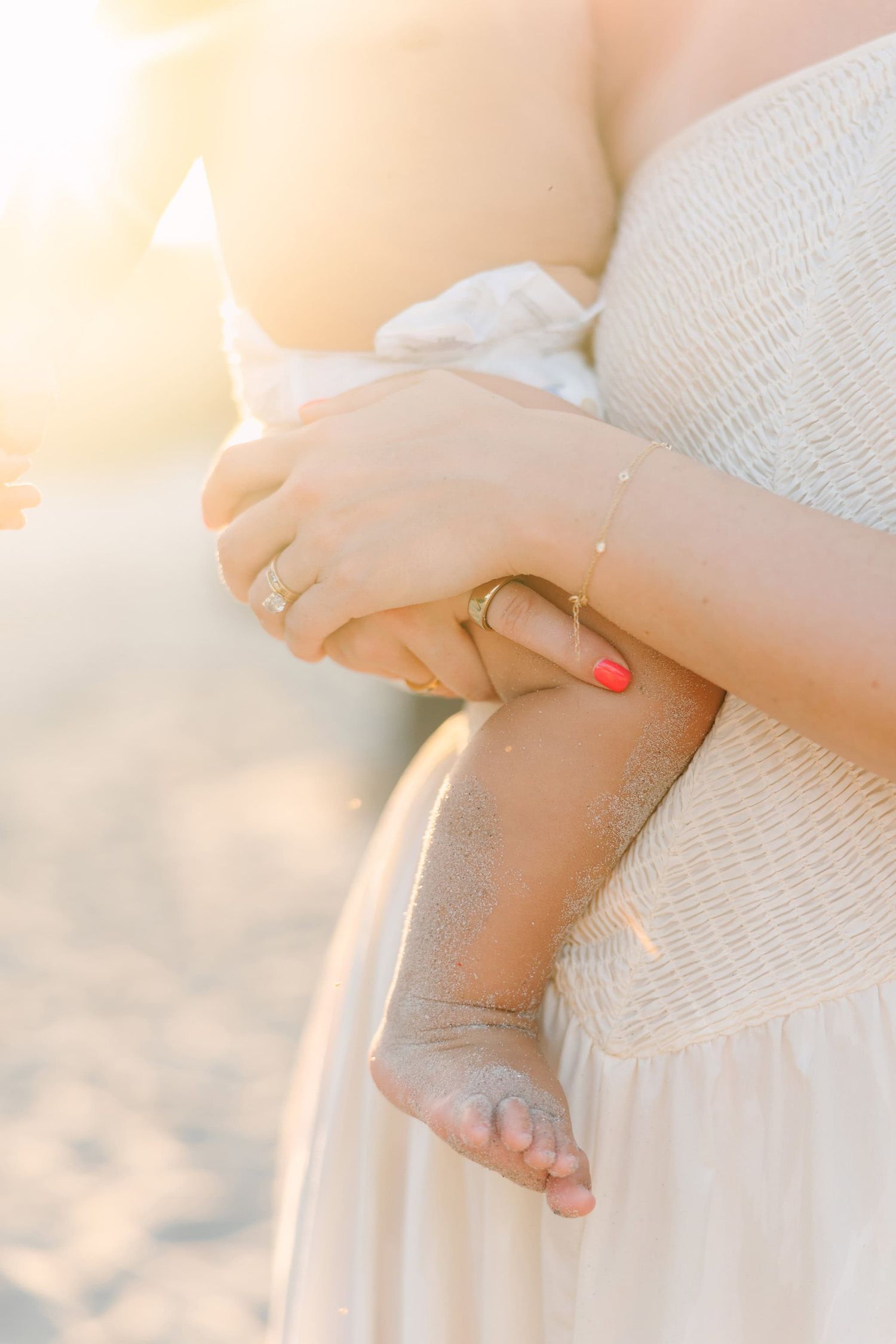 gorgeous sun flare over mom holding baby, close up of his sandy toes at the beach while sitting on her hip