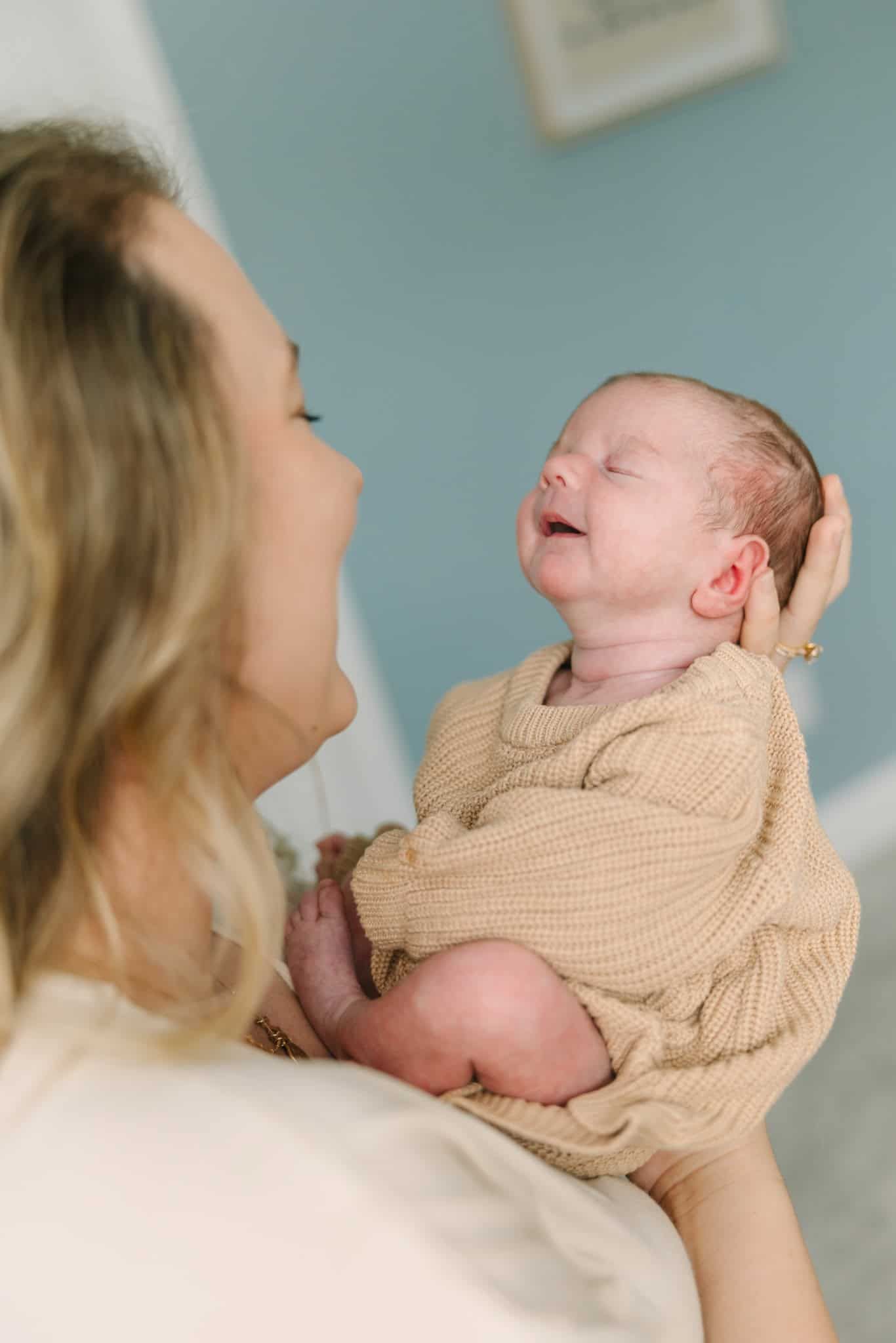 mom holding newborn baby boy out and he has a big smile on his face