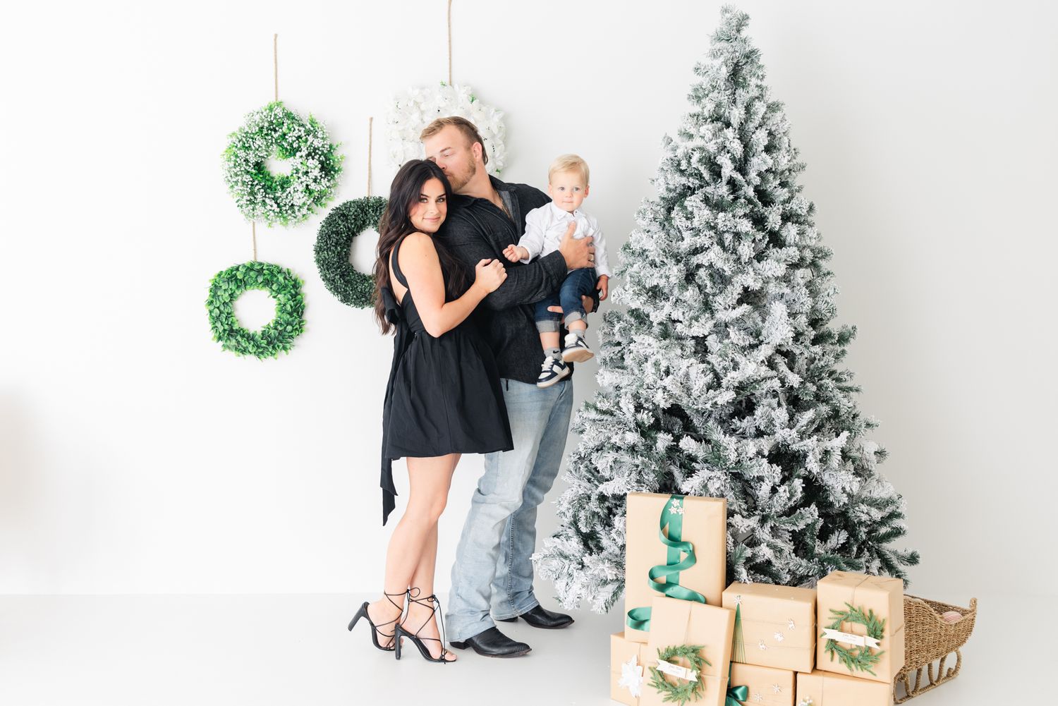 family smiling with dad kissing mom next to Christmas tree