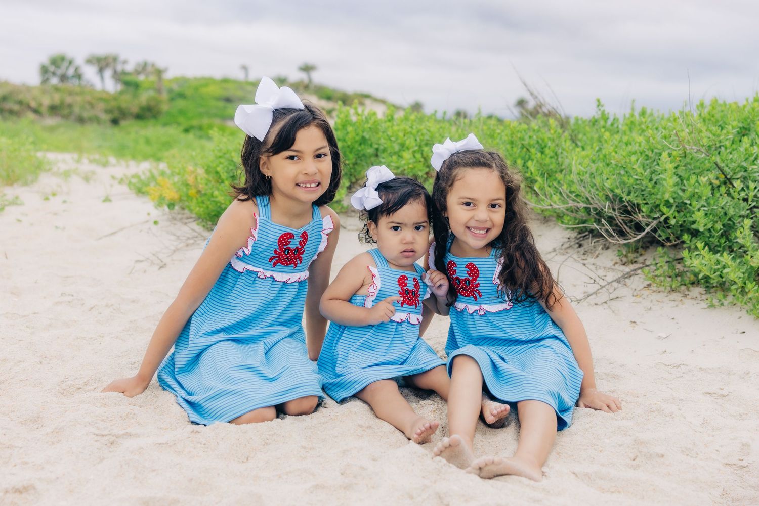 three daughters in matching dresses on the beach with a crab on the dress