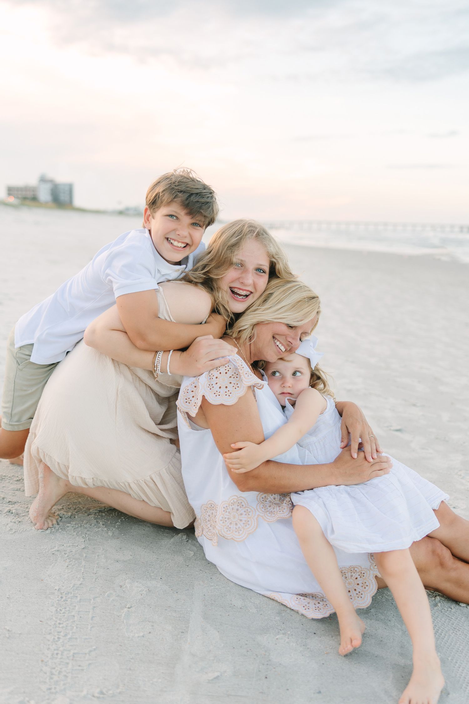 mom sitting in the sand in Jacksonville beach, fl with her 3 kids. all laughing and snuggling taken by Jacksonville fl photographer