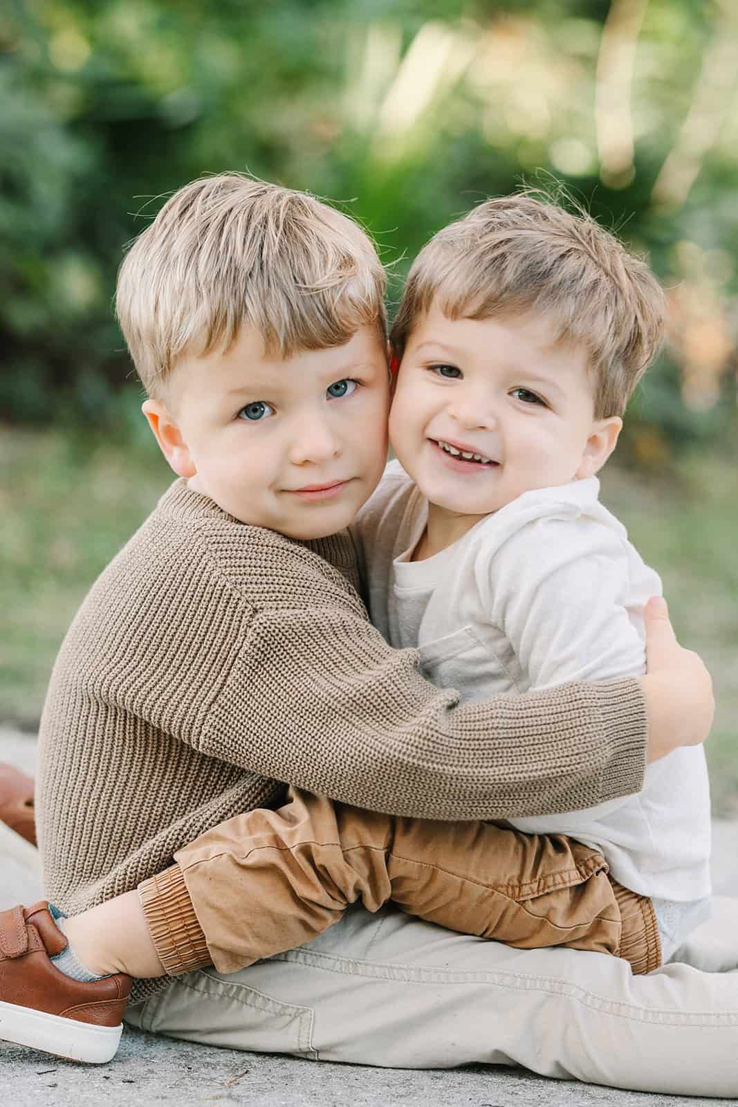 two toddler boys giving hug smiling at the camera