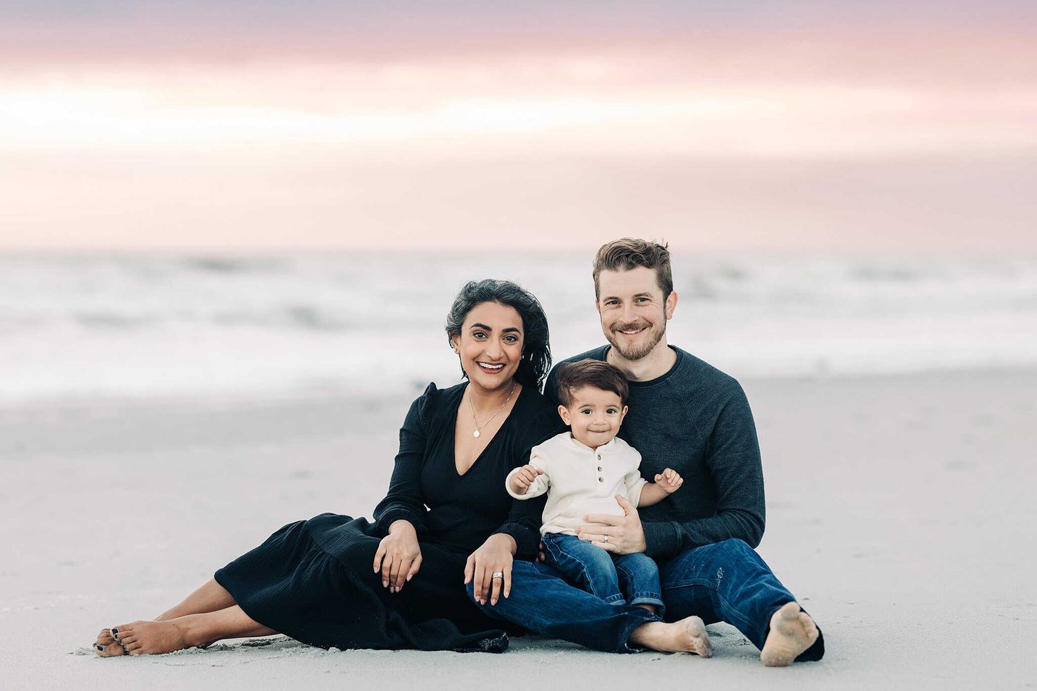family sitting in the sand in Jacksonville Beach with the sunrise coming up behind them