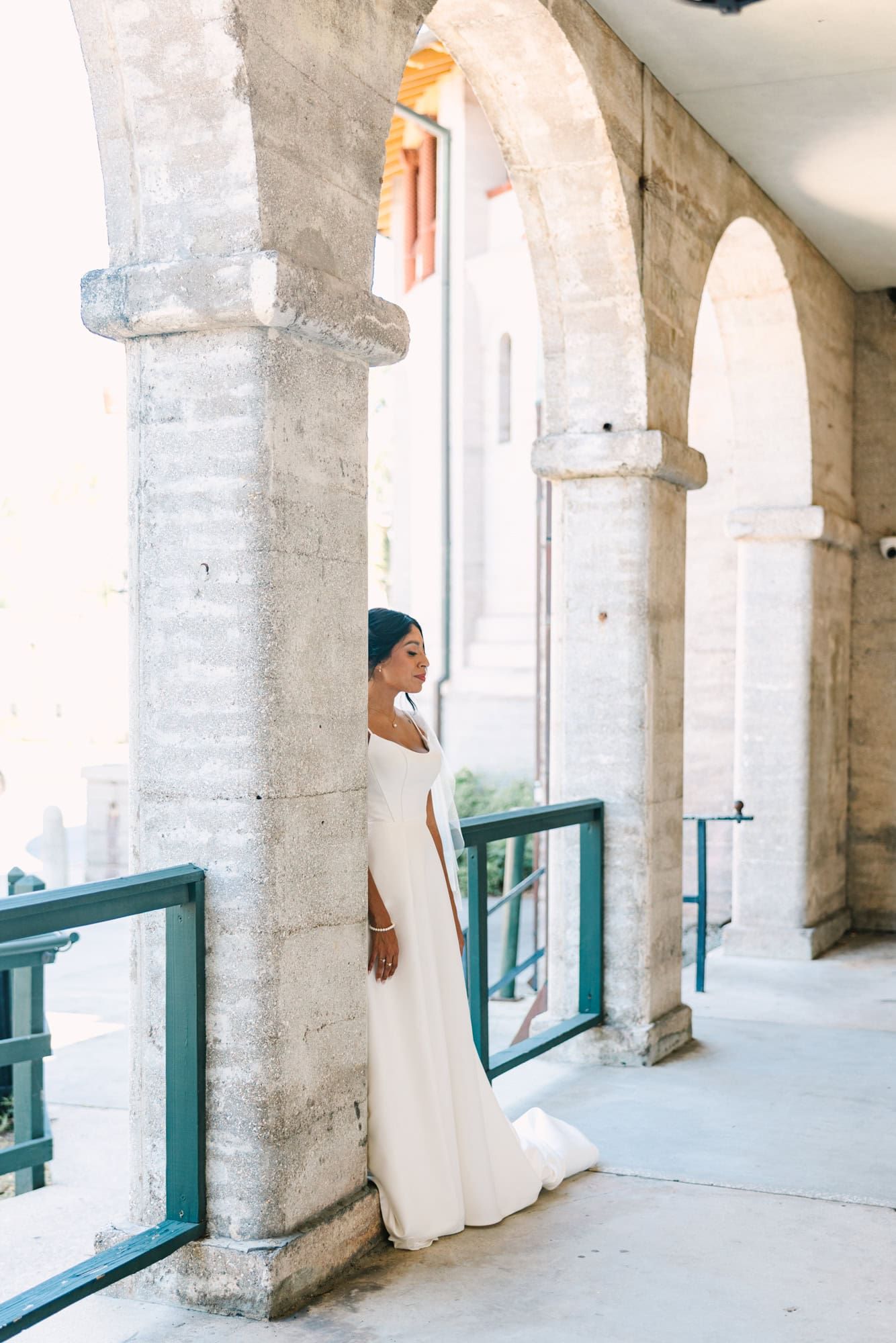 bride leaning on white brick under a big arch