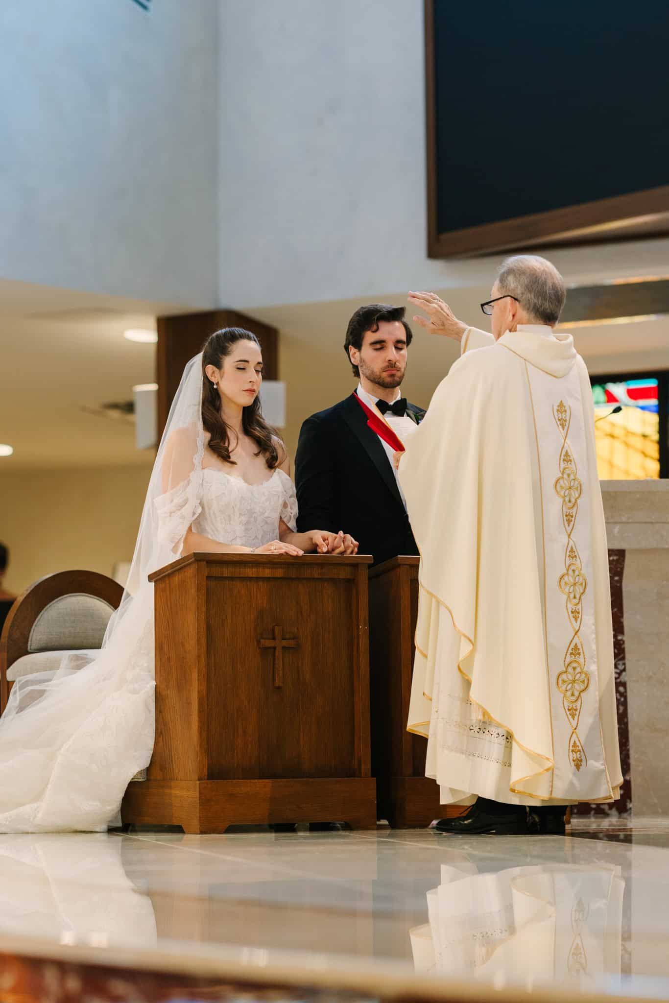 priest holding hand up in front of bride and groom during ceremony mass