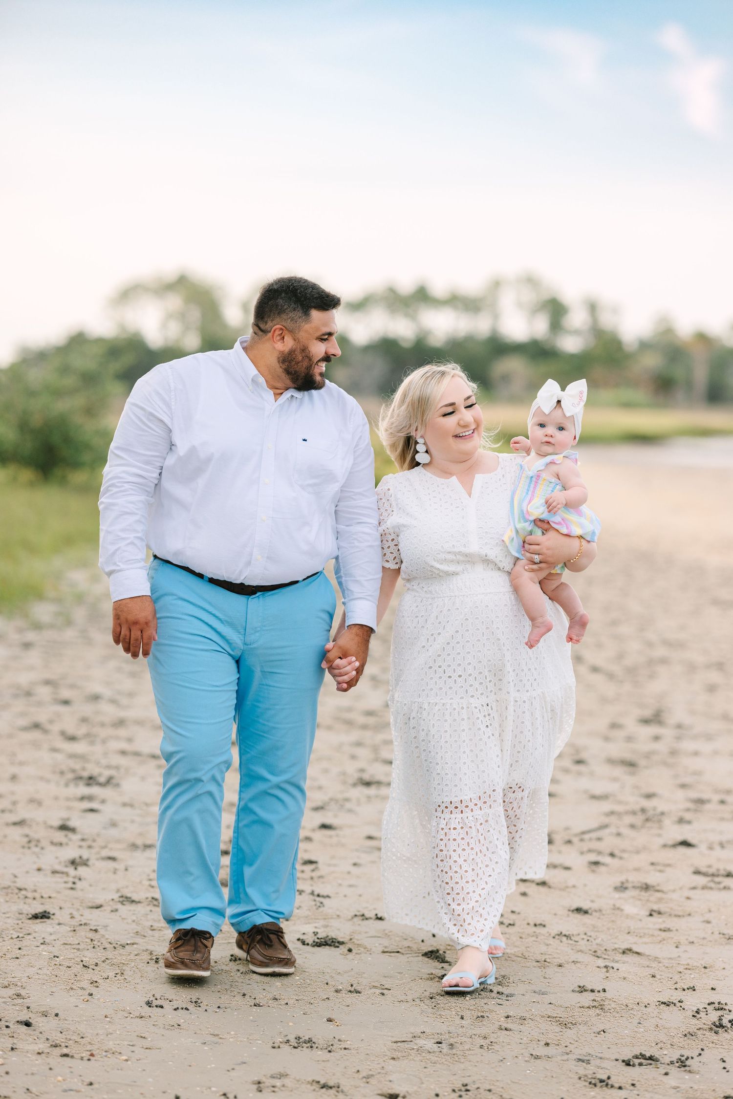 family walking down the beach holding baby girl with big cute bow
