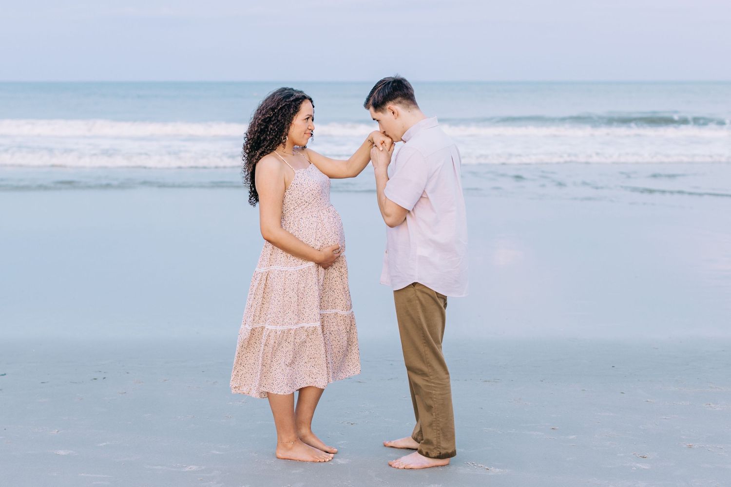 happy maternity couple on the beach with husband kissing wife's hand