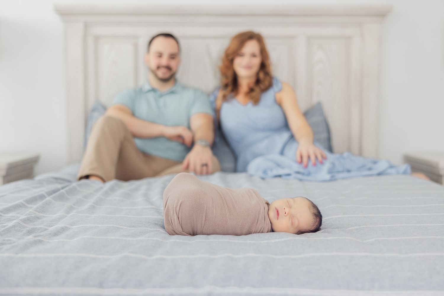 swaddled newborn baby in focus with parents smiling out of focus behind him