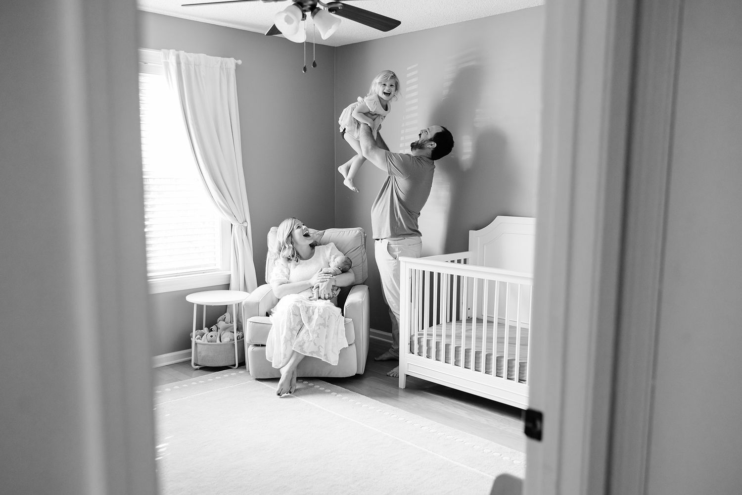family of 4 in black and white in nursery with mom holding baby and dad playing with toddler taken by Jacksonville, fl photographer