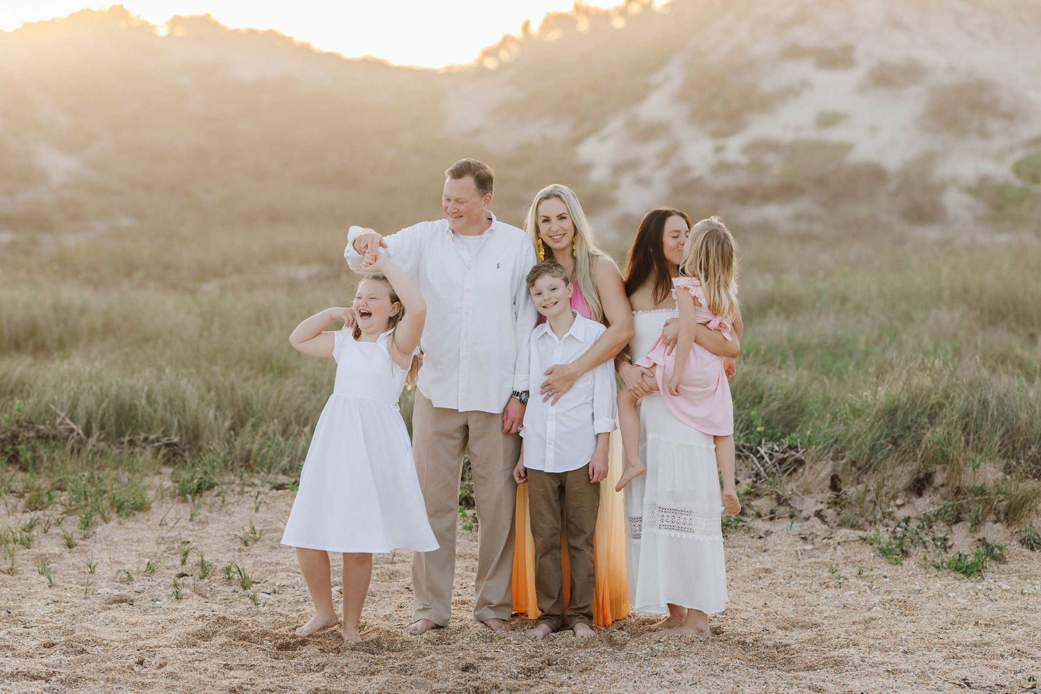 snuggling on the beach at sunset, dad is twirling daughter and other kids are hugging