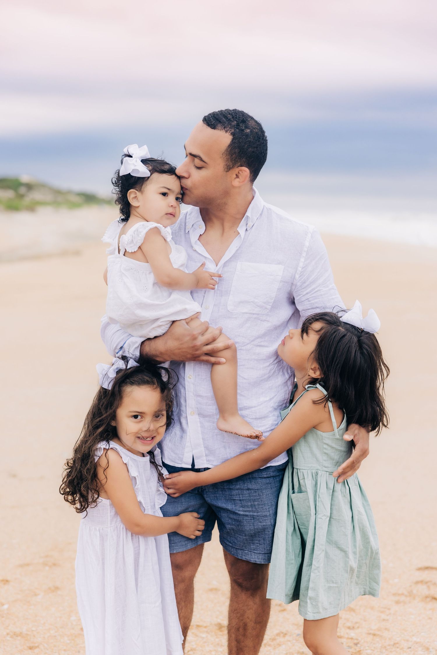 dad kissing youngest daughter and older two hugging dad on jacksonville beach fl