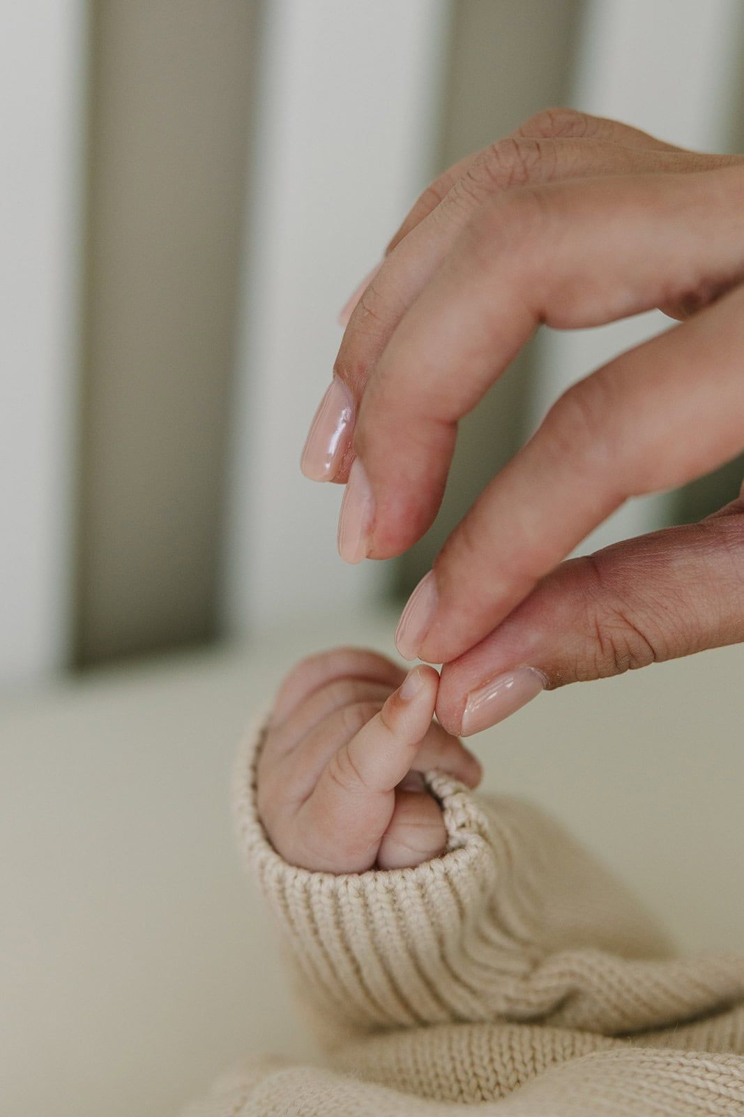 Mama's hand gently holding her newborn baby's tiny finger wrapped in a soft cream knit sweater sleeve.