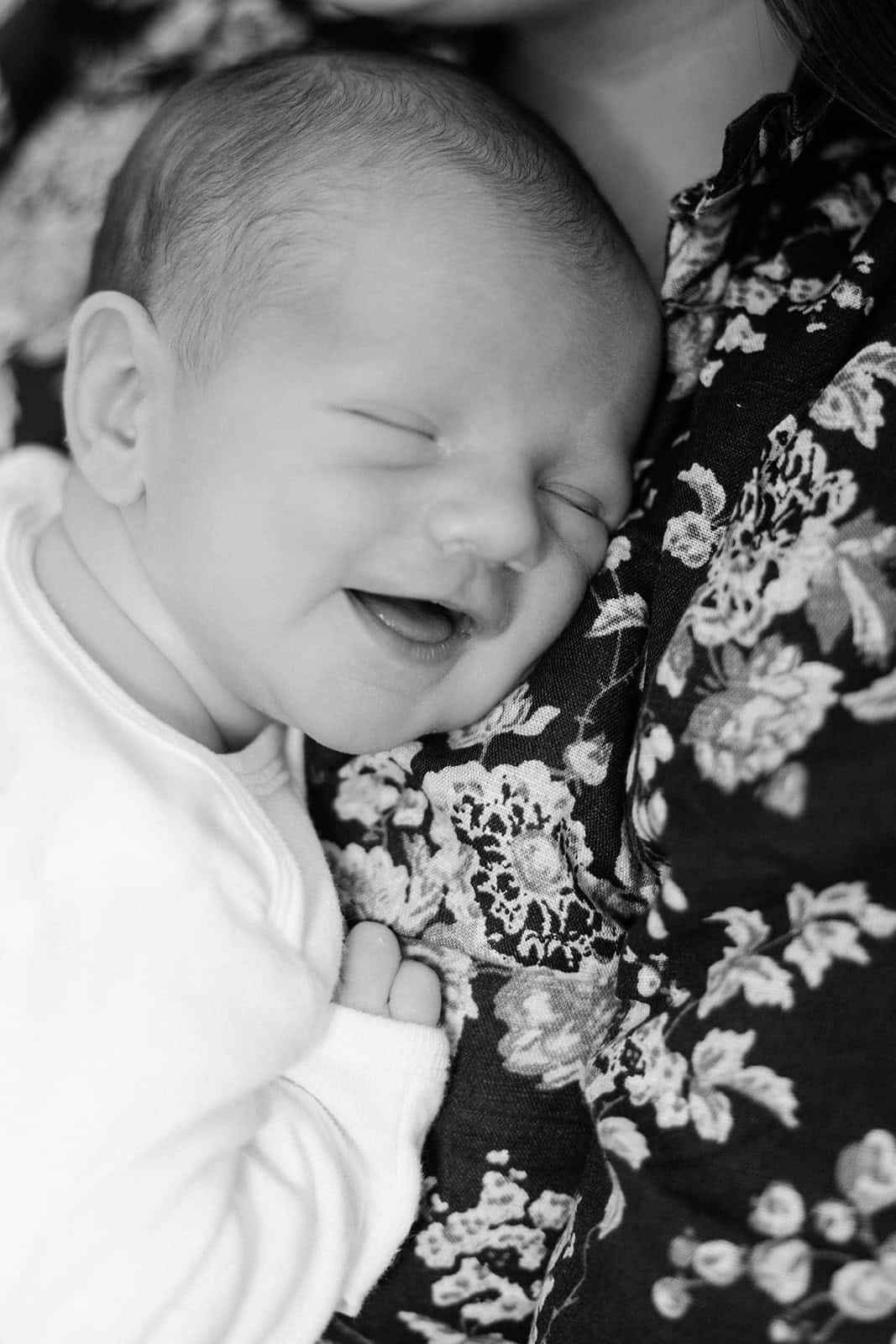 black and white photo of newborn baby laying on moms chest with a big smile