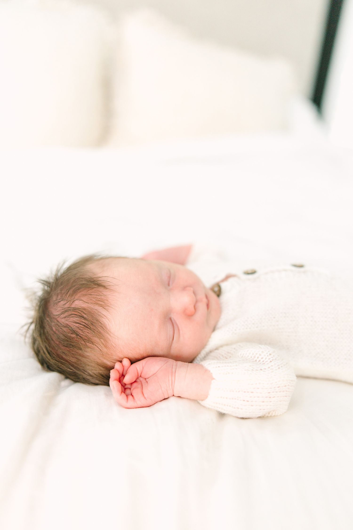 newborn baby laying on the white bed with little hand up by his face
