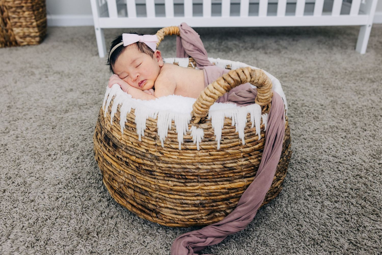 newborn baby girl in a basket with pink swaddle draped gently over her