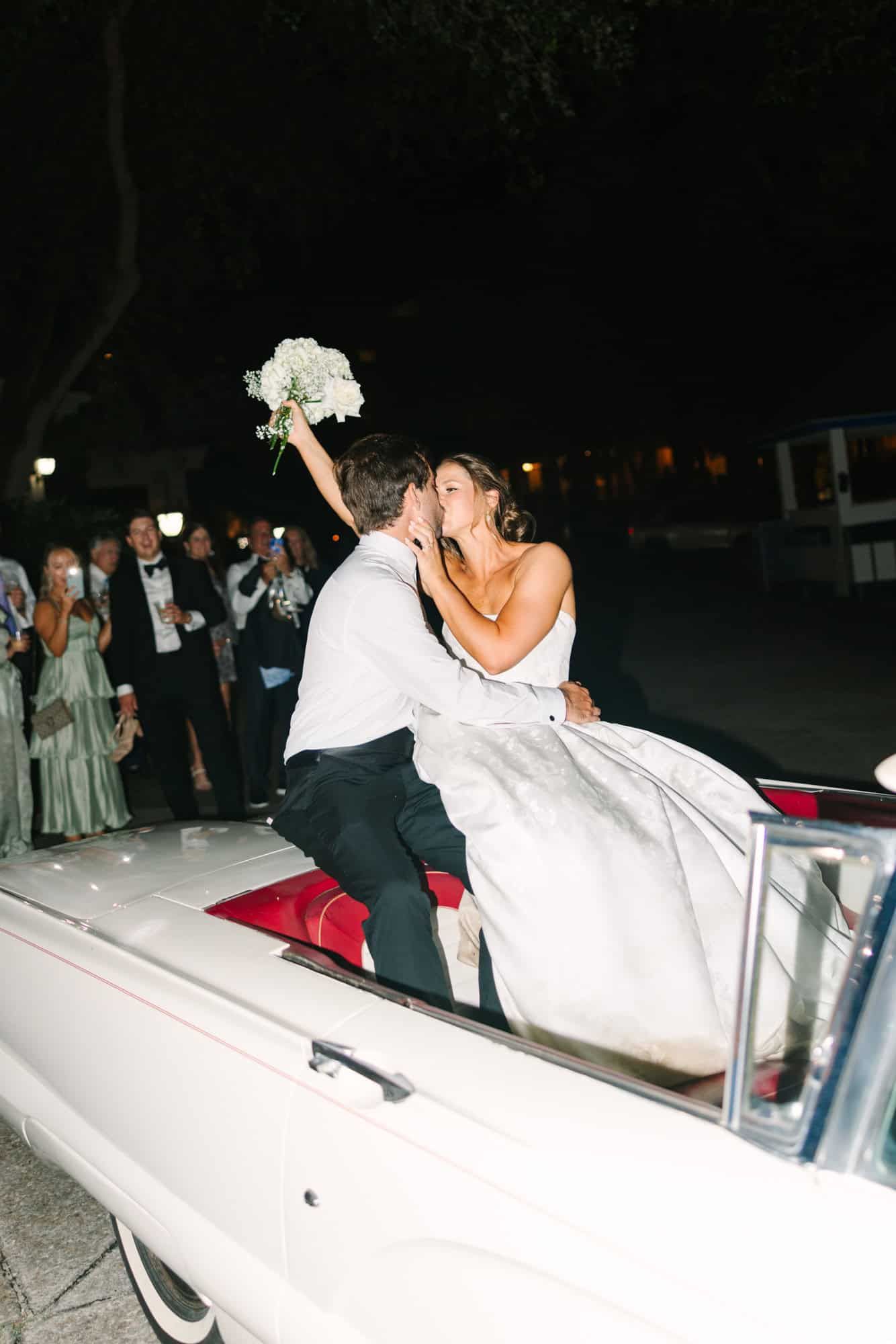 bride and groom kissing sitting on the back of a fancy white car during their exit