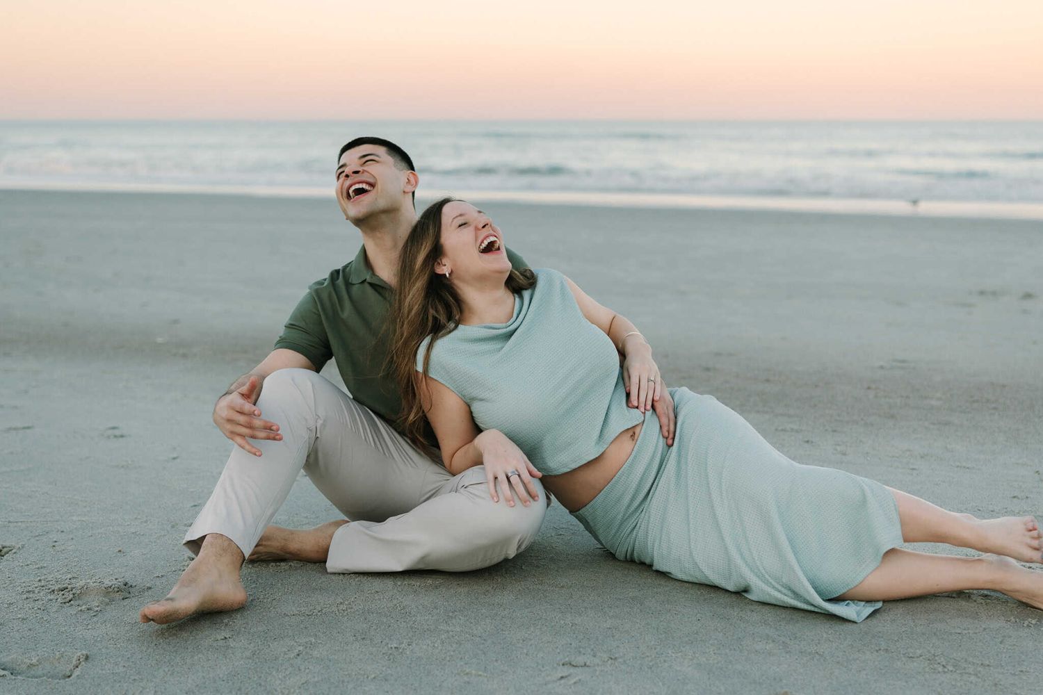 pregnant couple laughing on the beach at sunset