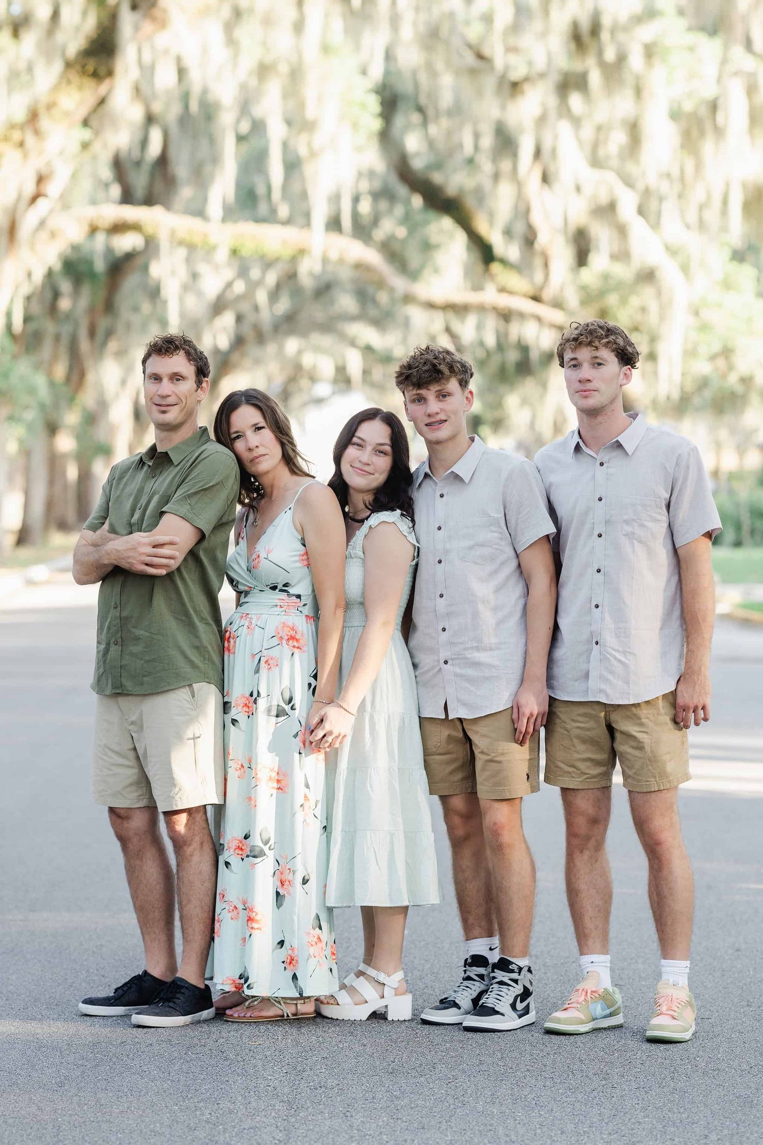 family of five with adult children standing and smiling with canopy trees over them