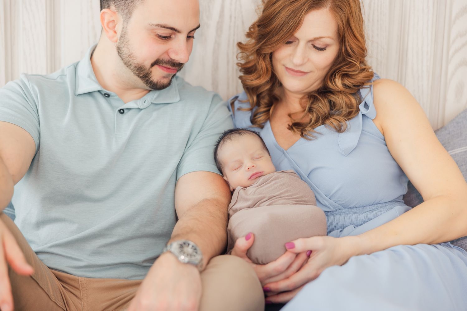 mom and dad holding newborn baby swaddled for photographer