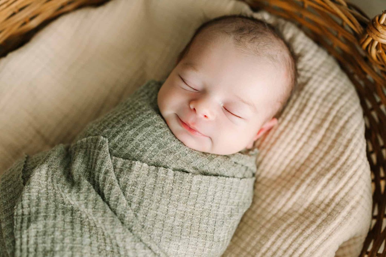 newborn baby boy swaddled in a basket with a little smile on his face