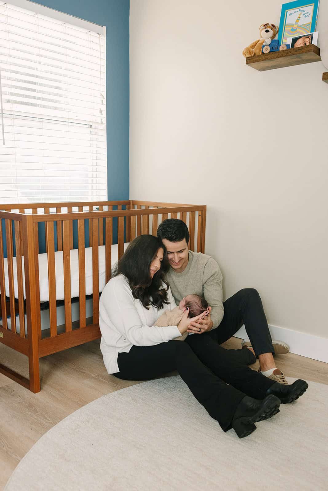 mom and dad sitting in front of crib in nursery looking at newborn baby in st Augustine fl