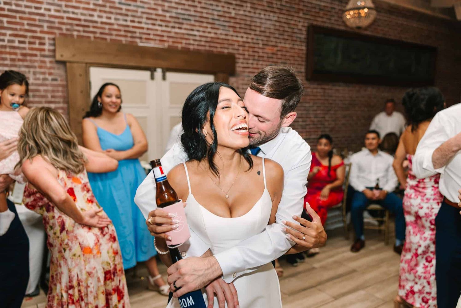 Couple embracing and dancing joyfully at a wedding reception in a rustic brick venue.