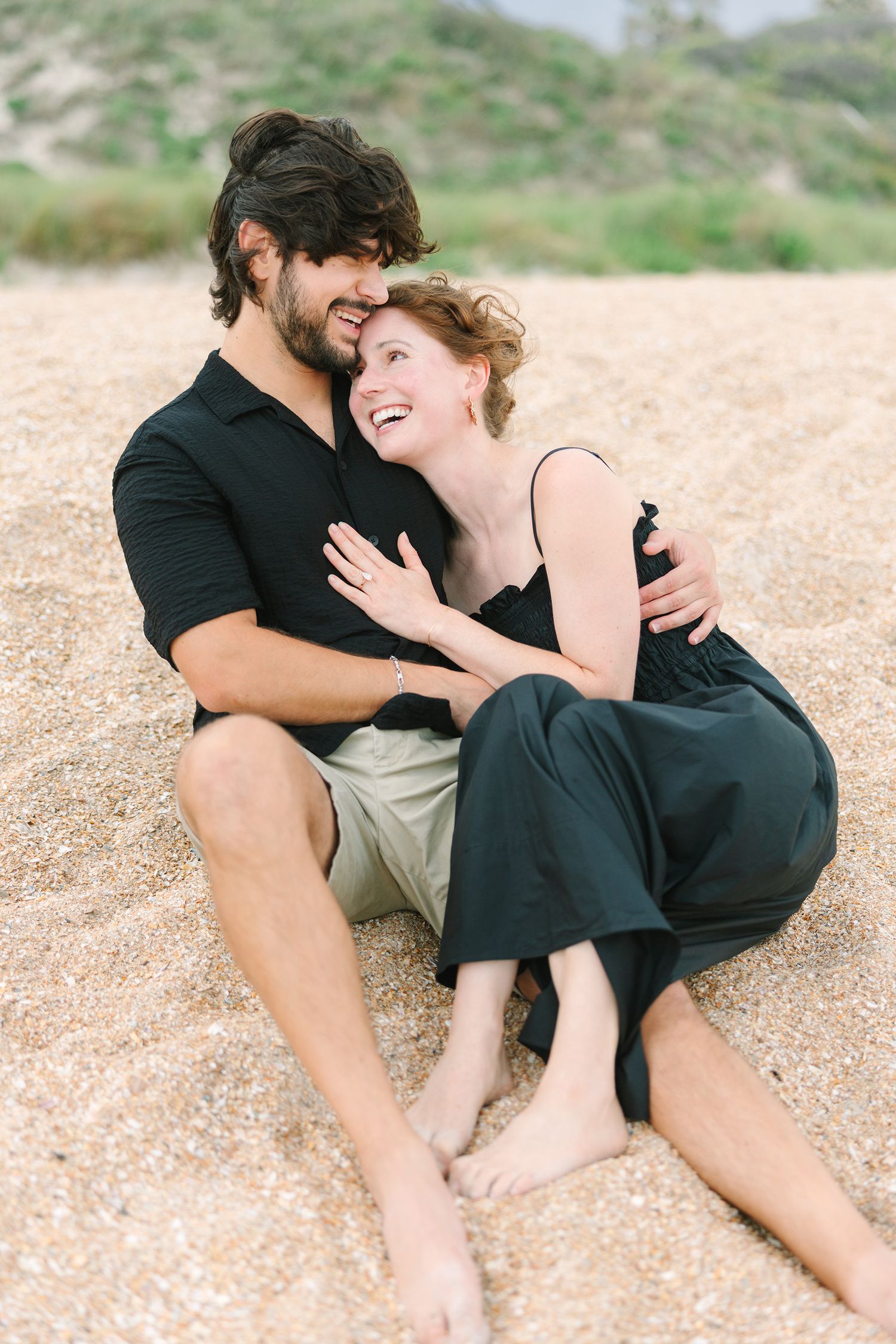 couple sitting in the sand laughing and snuggling at Jacksonville beach, fl